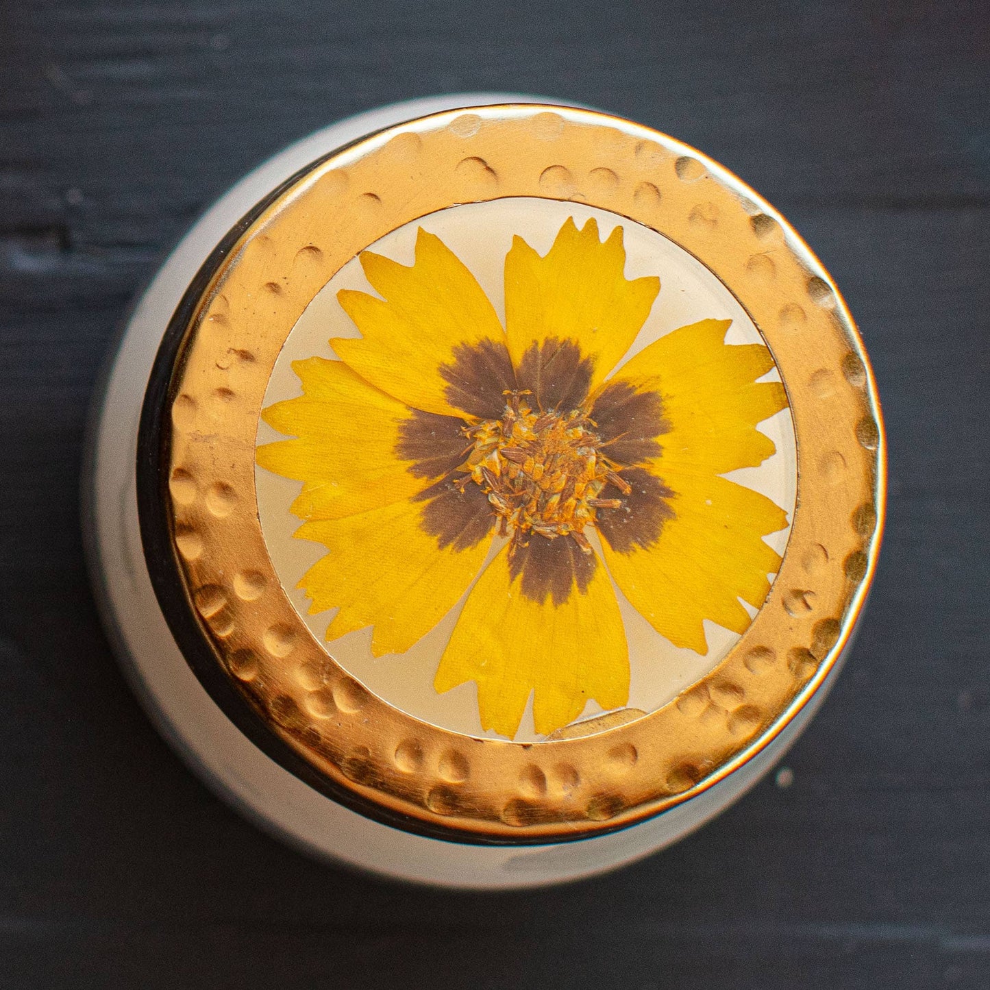 Round decorative item with a yellow flower in the center on a dark background