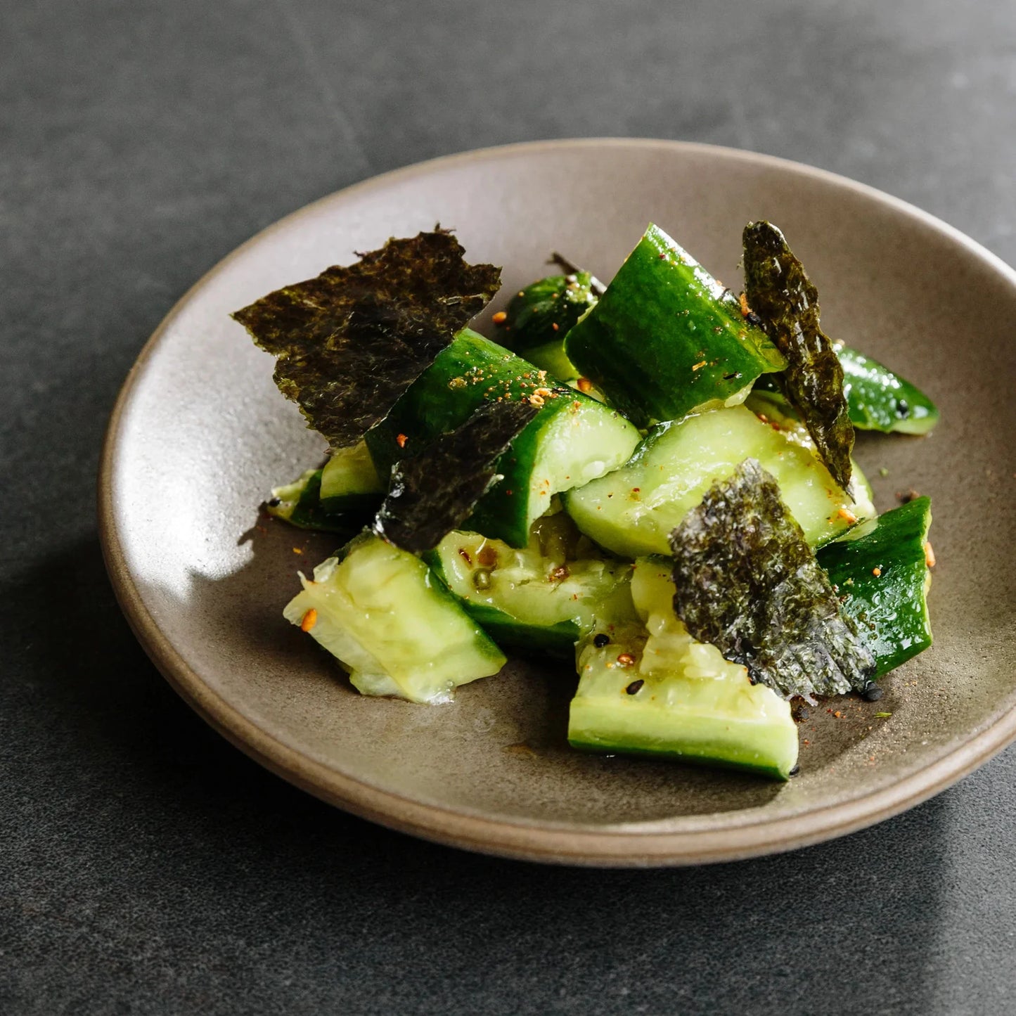 Cucumber salad with seaweed on a brown plate against a dark background