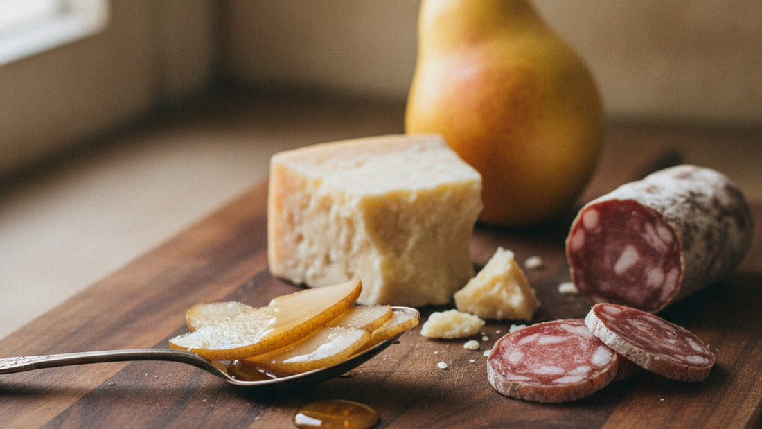Translucent slices of candied pear glistening in syrup on a small spoon beside a craggy chunk of aged grana cheese and thin slices of salame on a wooden board