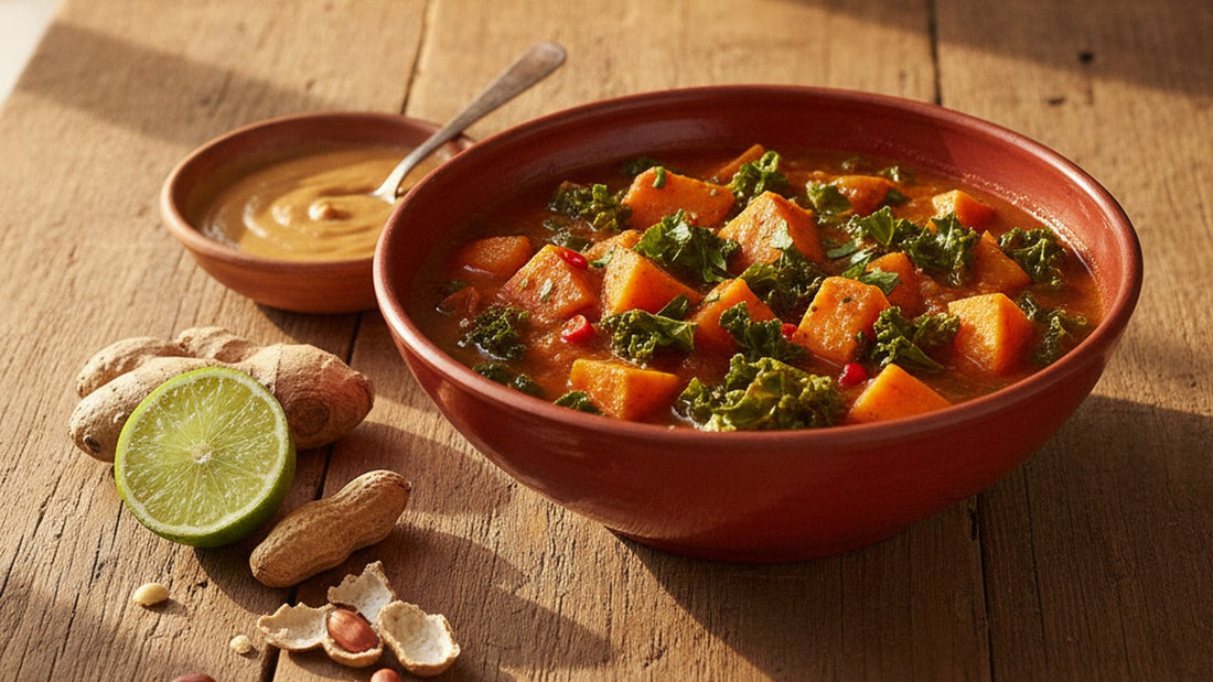 A bowl of peanut stew with sweet potato and dark greens beside a small dish of glossy peanut sauce and a scatter of roasted peanuts on a wooden table