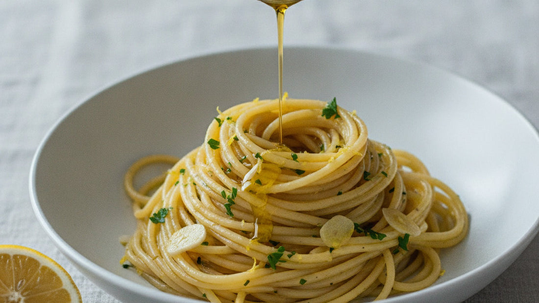 A shallow bowl of spaghetti glossy with olive oil and flecked with parsley and lemon zest, a small spoon pouring amber colatura over the top
