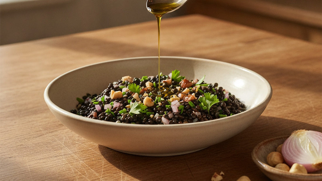 A shallow bowl of glossy warm black lentils with diced shallot, chopped toasted hazelnuts and parsley, a thread of golden nut oil being poured over the top