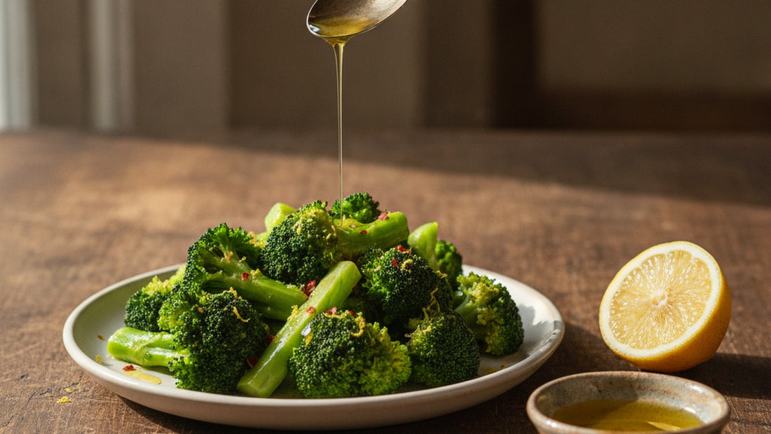 A shallow platter of bright green steamed broccoli glistening with olive oil and lemon zest, a spoon dripping amber colatura over the florets