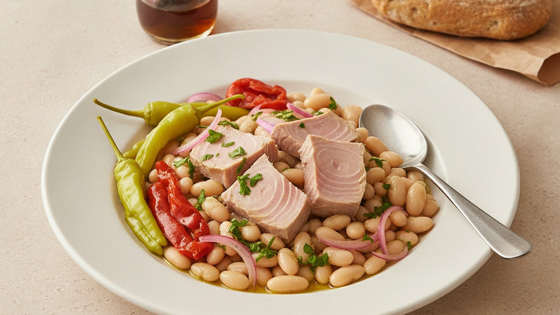 A wide platter of creamy white beans glossy with olive oil, topped with large soft pieces of pale pink tuna belly, long green piparra peppers, red onion and parsley
