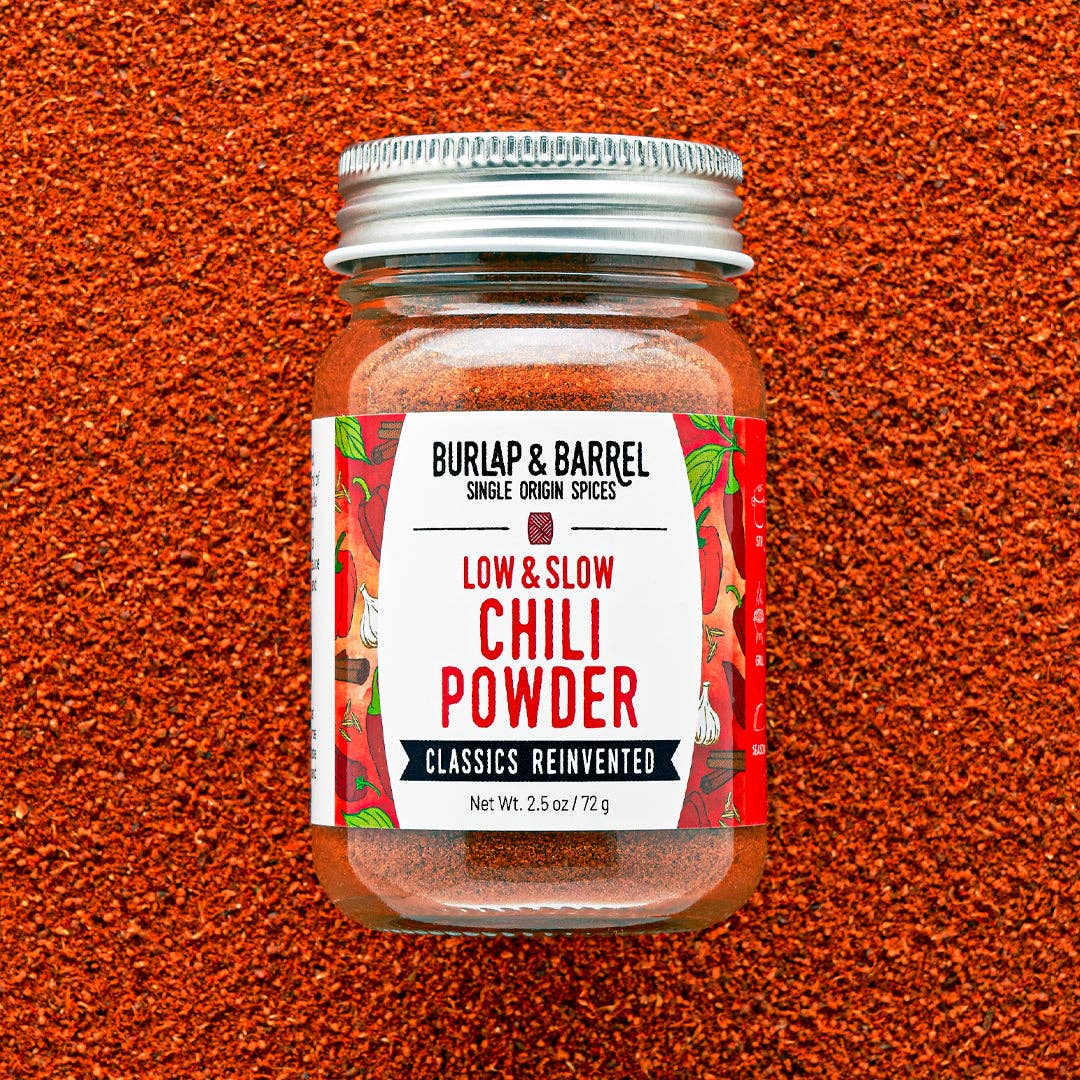 Jar of Burlap & Barrel Low & Slow Chili Powder on a textured red background