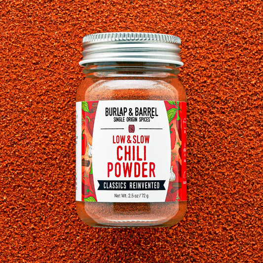 Jar of Burlap & Barrel Low & Slow Chili Powder on a textured red background