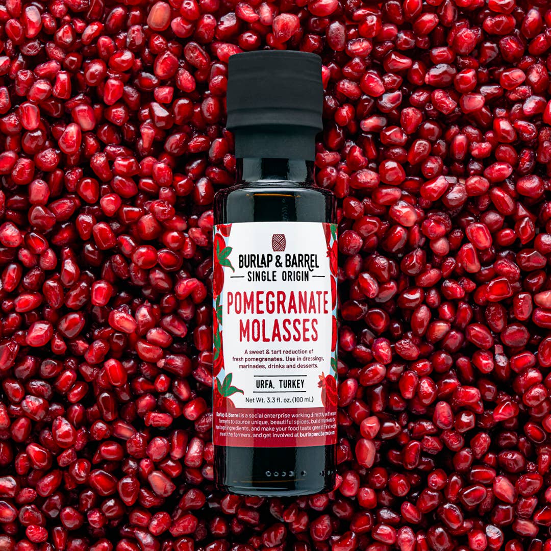 Bottle of Burlap & Barrel Pomegranate Molasses against a background of pomegranate seeds