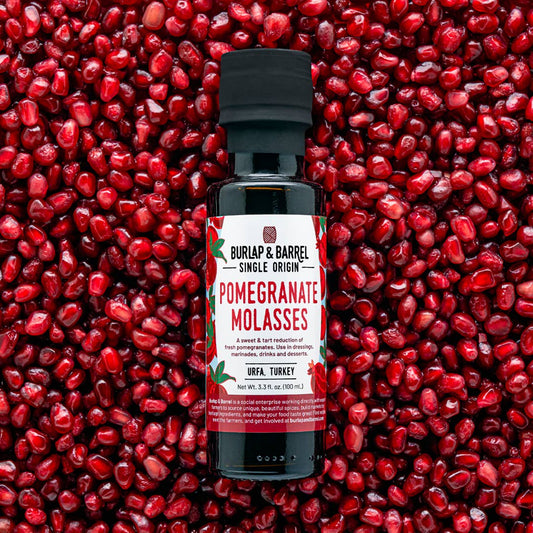 Bottle of Burlap & Barrel Pomegranate Molasses against a background of pomegranate seeds