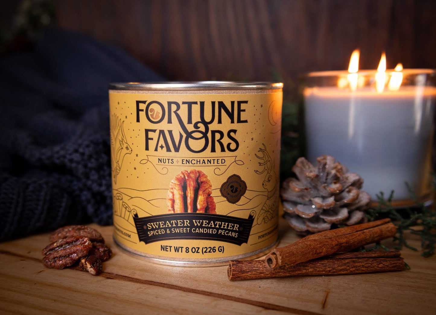 Can of 'Fortune Favors' nuts with a candle and pinecones on a wooden surface