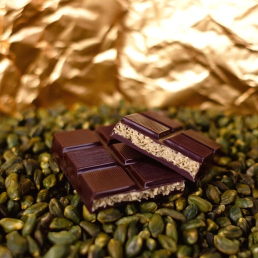 Chocolate bar with a crumbly center on green seeds with gold leaf in the background