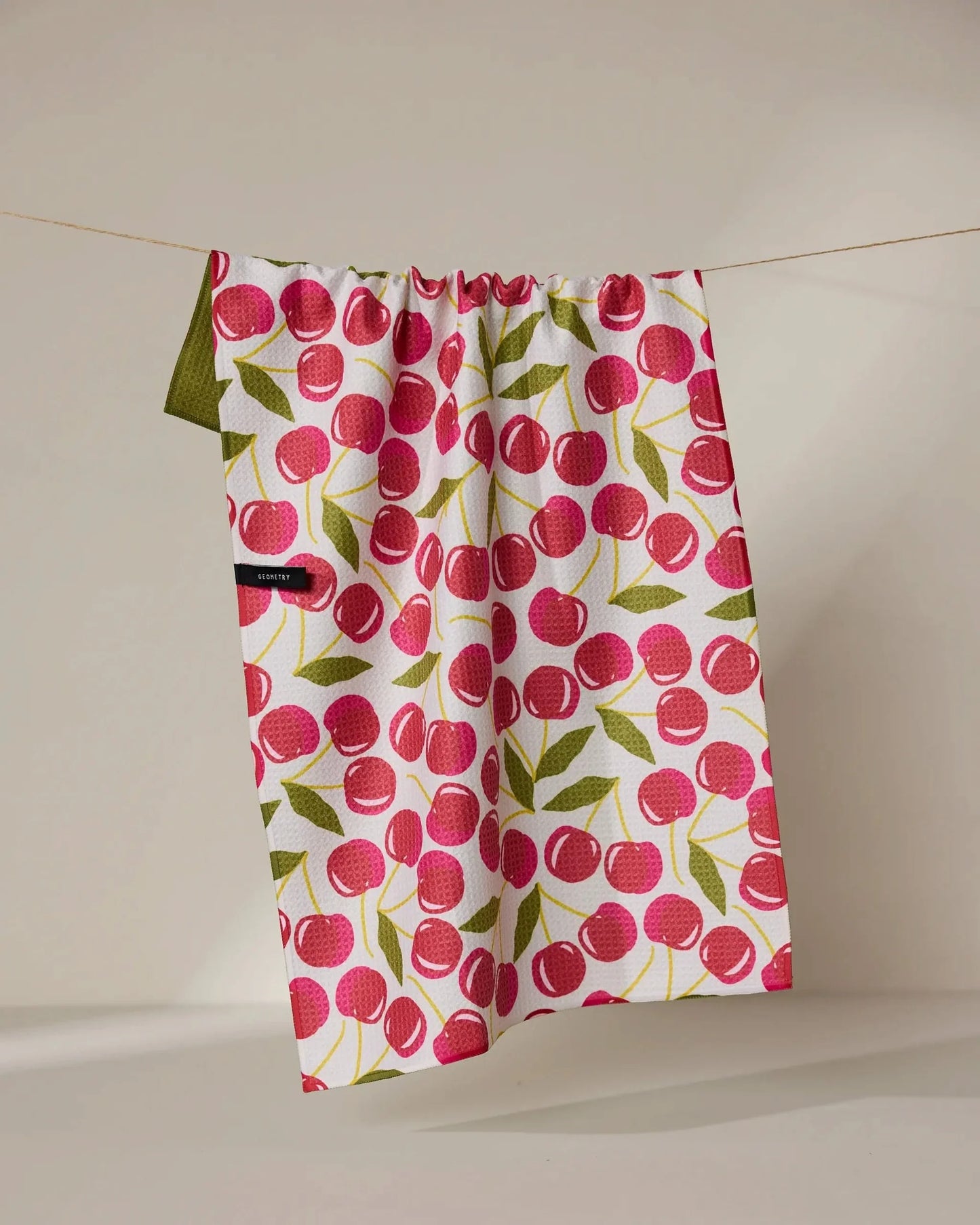 Fabric with cherry pattern hanging on a line against a beige background