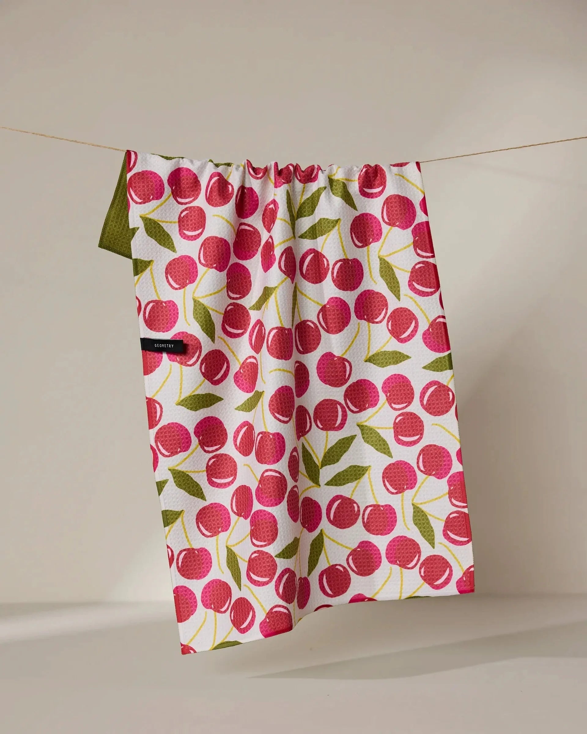 Fabric with cherry pattern hanging on a line against a beige background