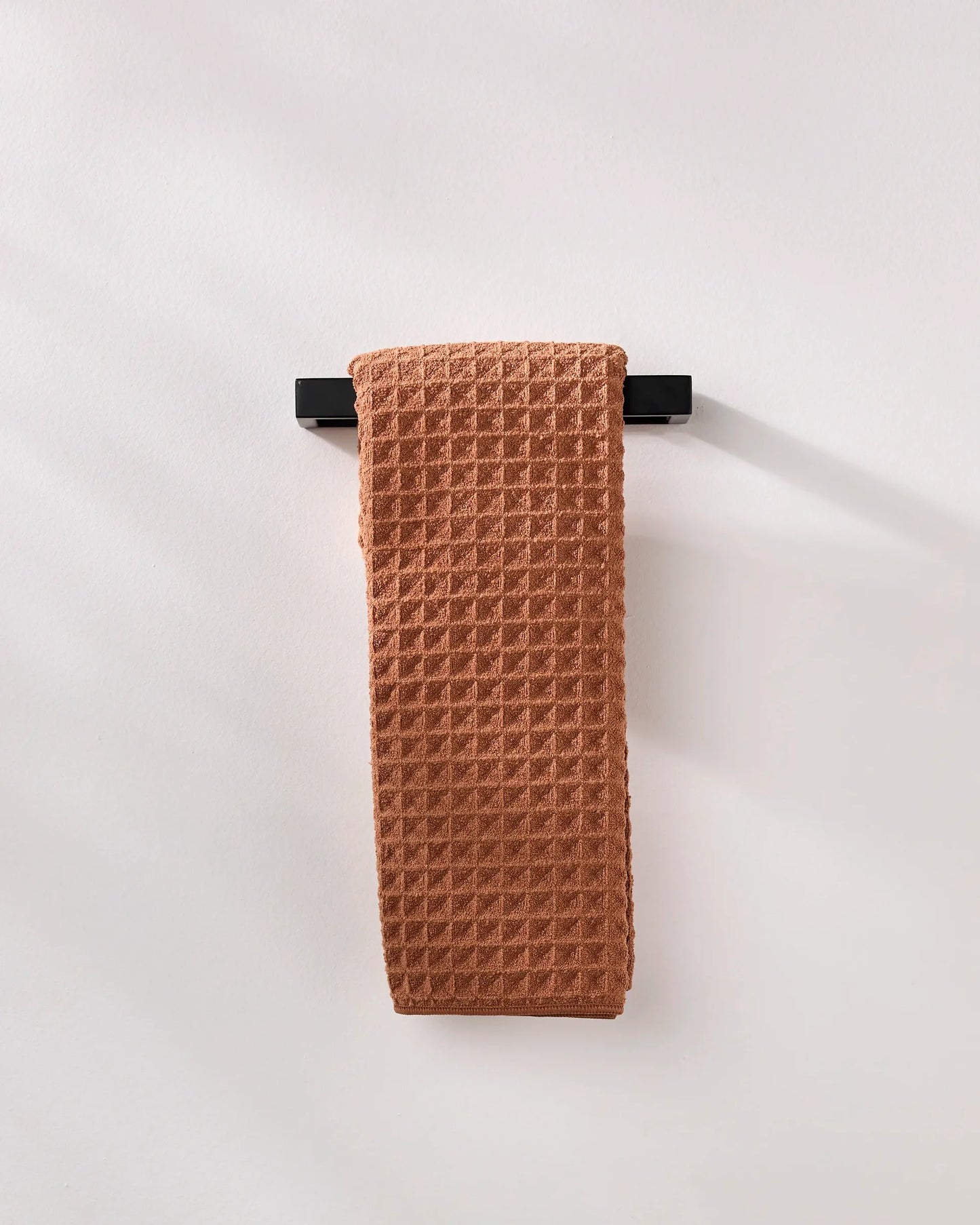 Brown textured towel hanging on a black rack against a white background