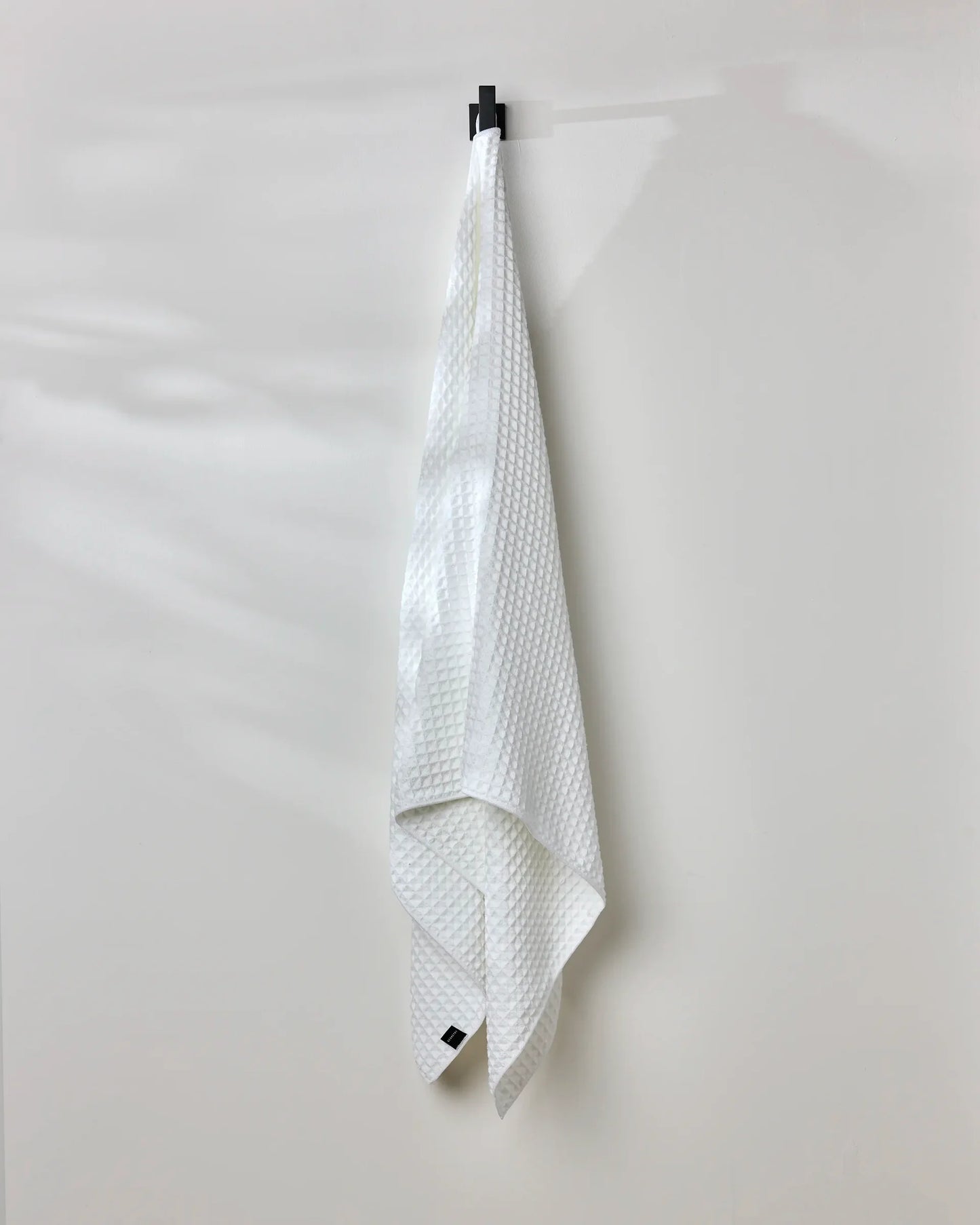 White textured towel hanging on a black clip against a white background