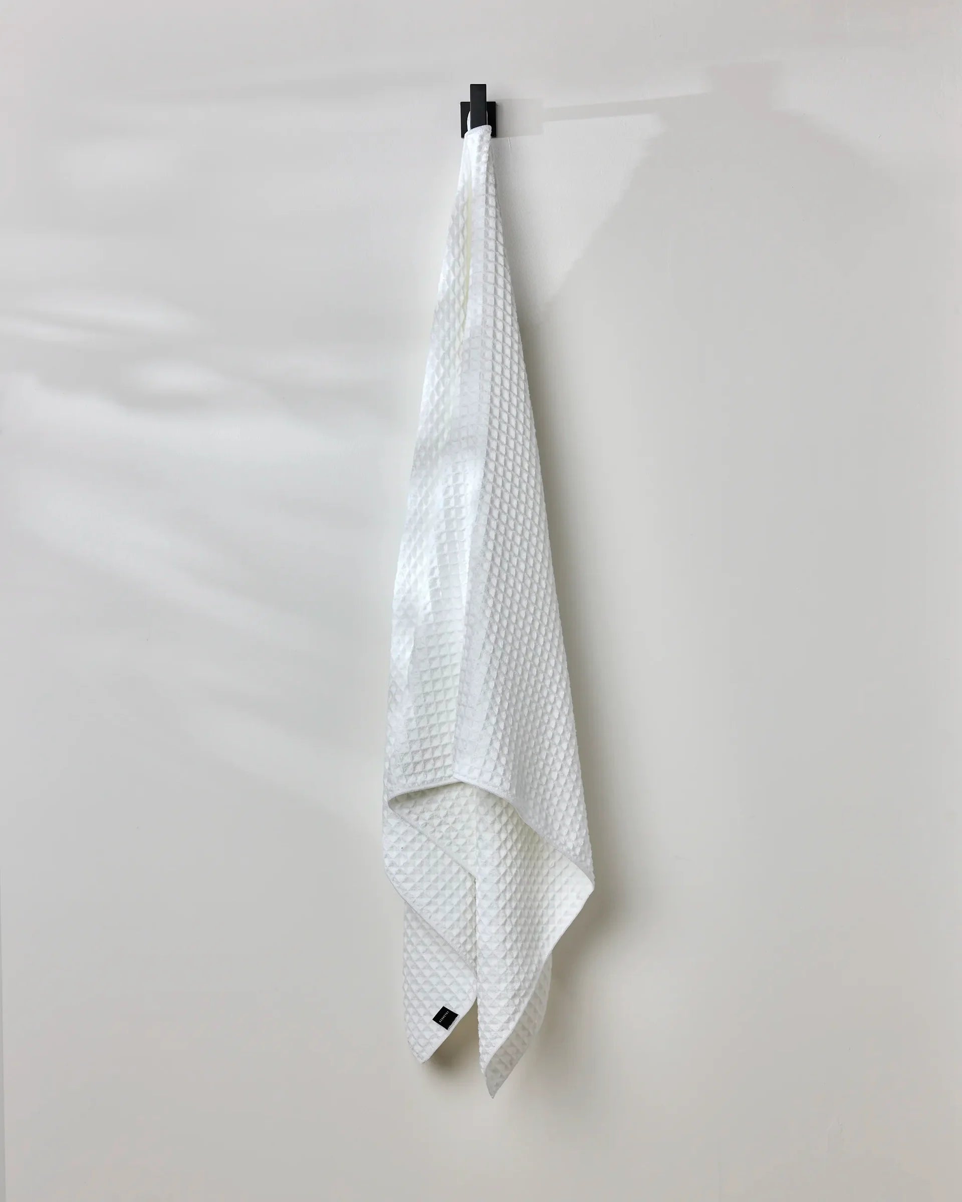 White textured towel hanging on a black clip against a white background