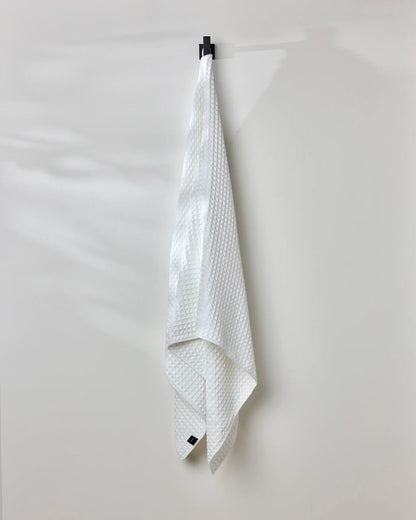 White textured towel hanging on a black clip against a white background
