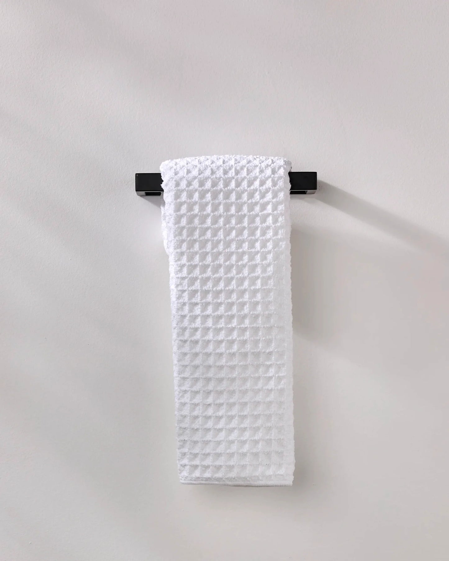 White textured towel hanging on a black rack against a light gray background