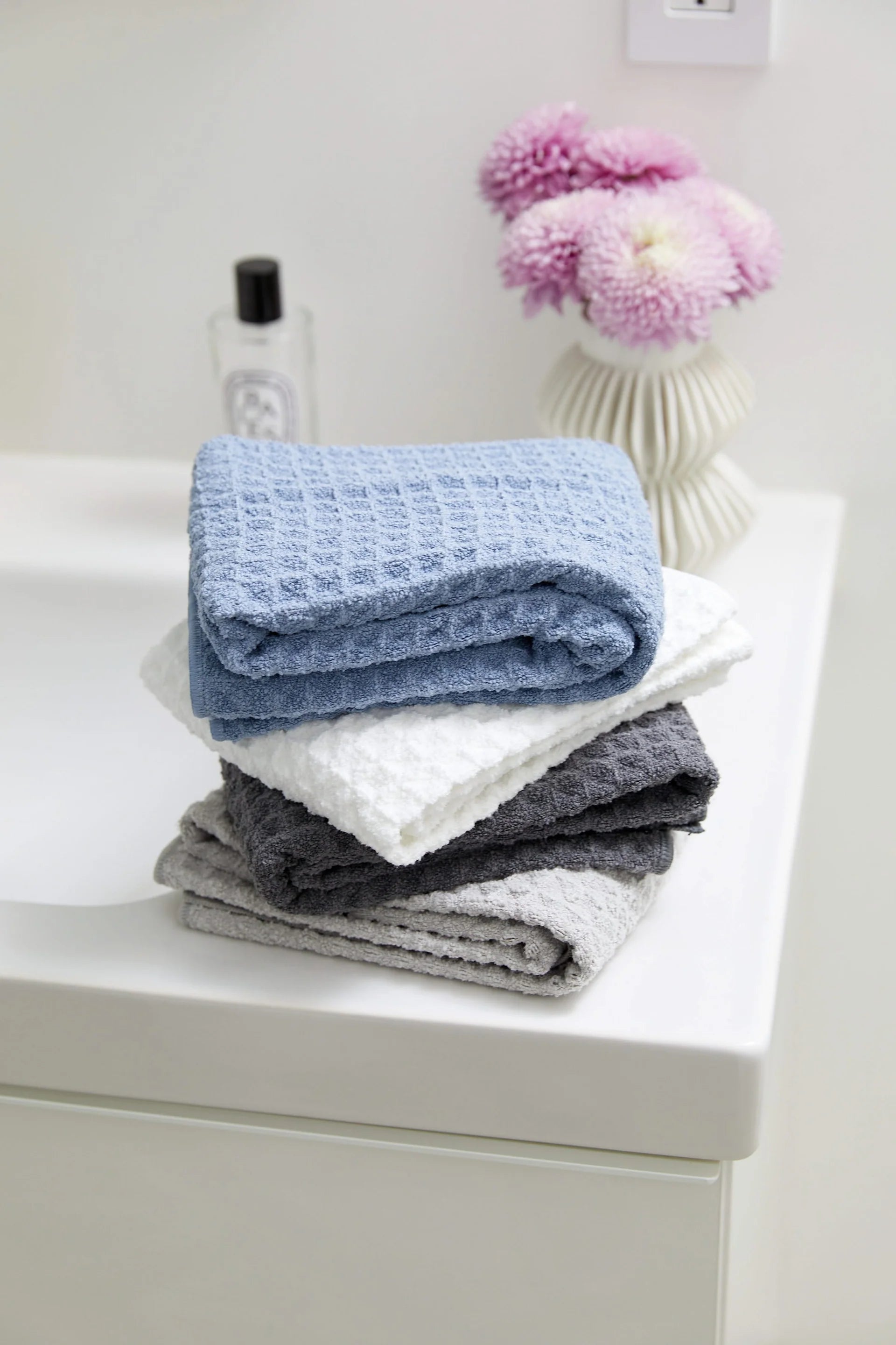 Stack of folded towels in blue, white, and gray on a white surface with a small plant in the background.