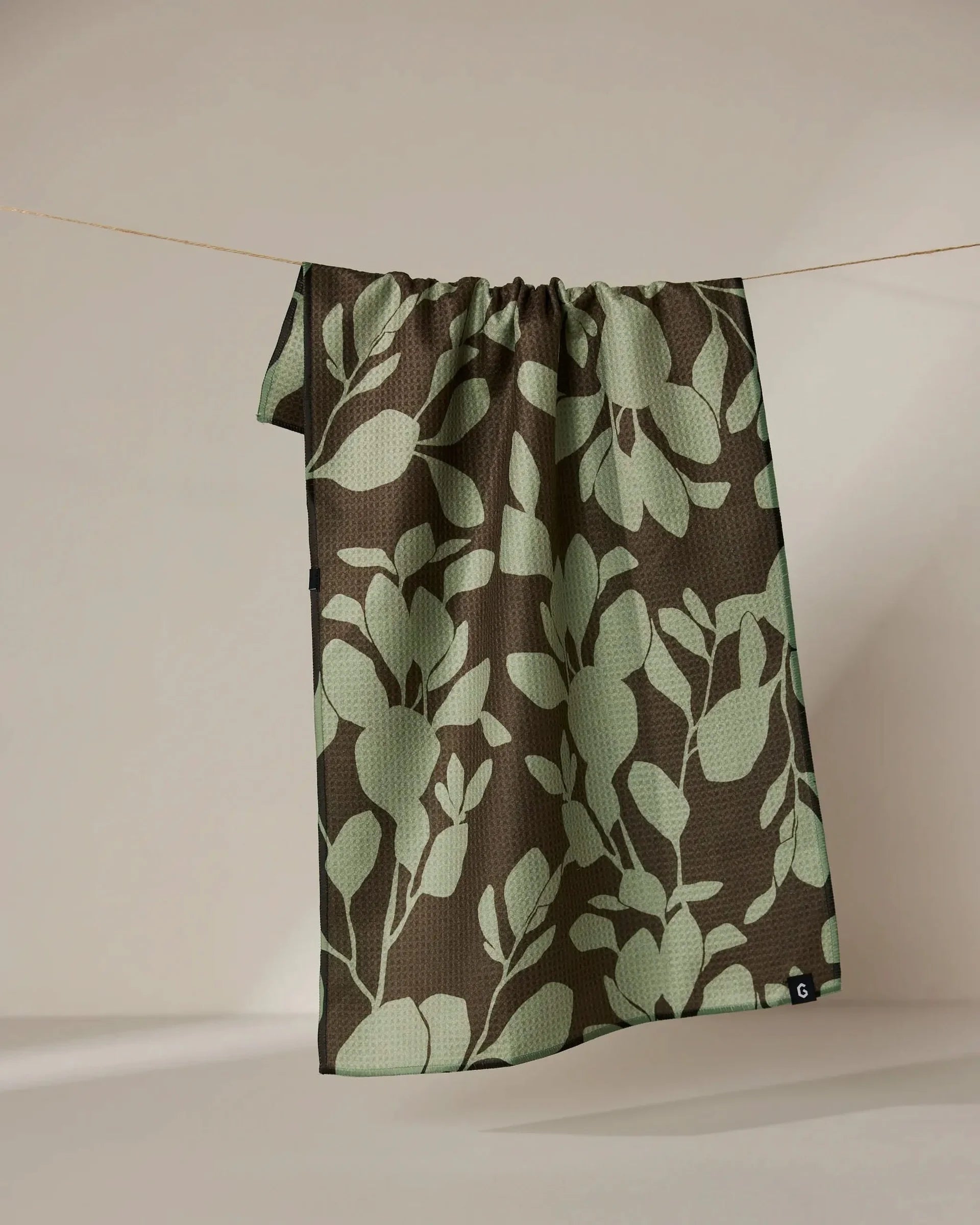 Fabric with green leaf pattern on a brown background, hanging against a plain wall.