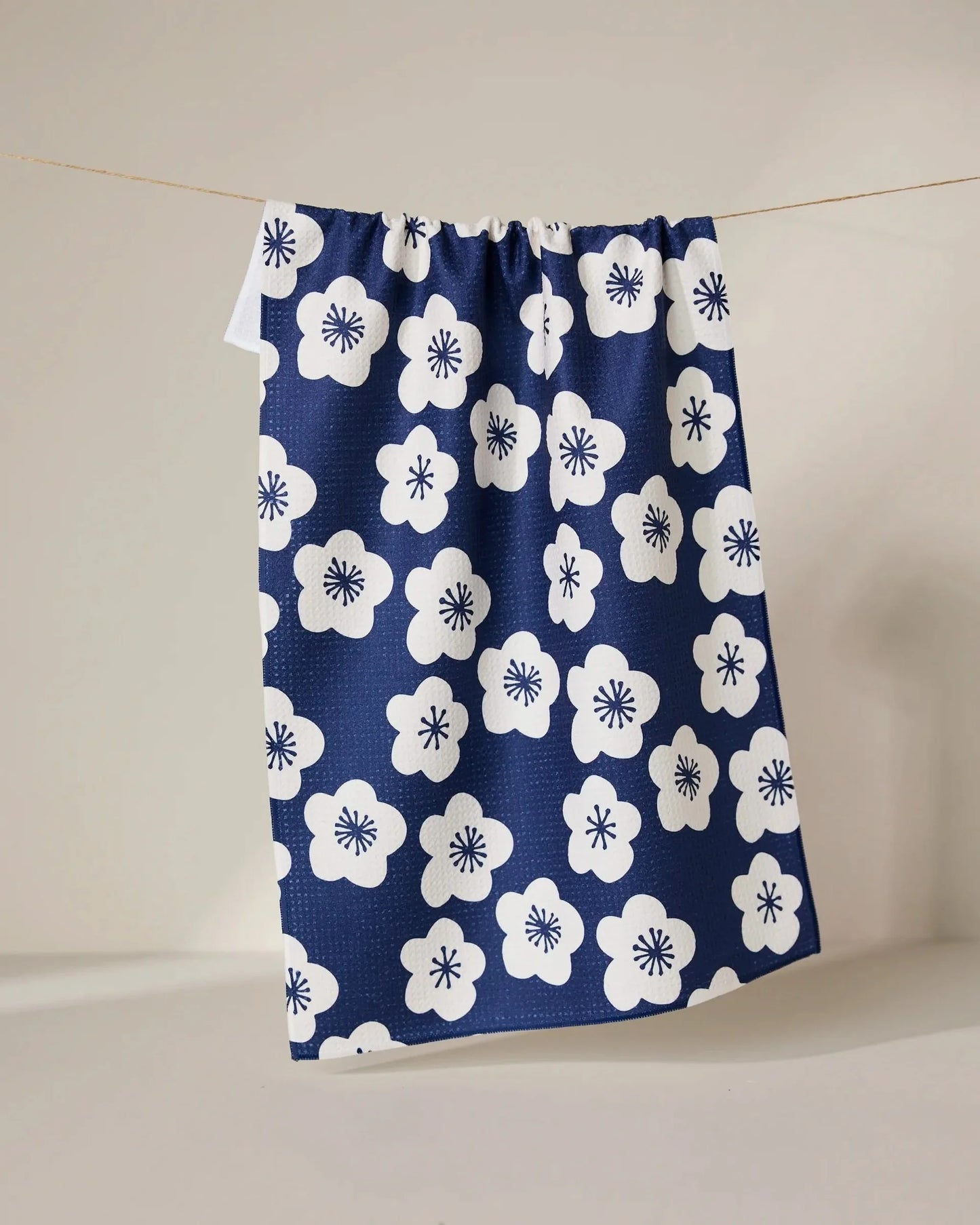 Navy blue towel with white floral pattern hanging on a line against a neutral background