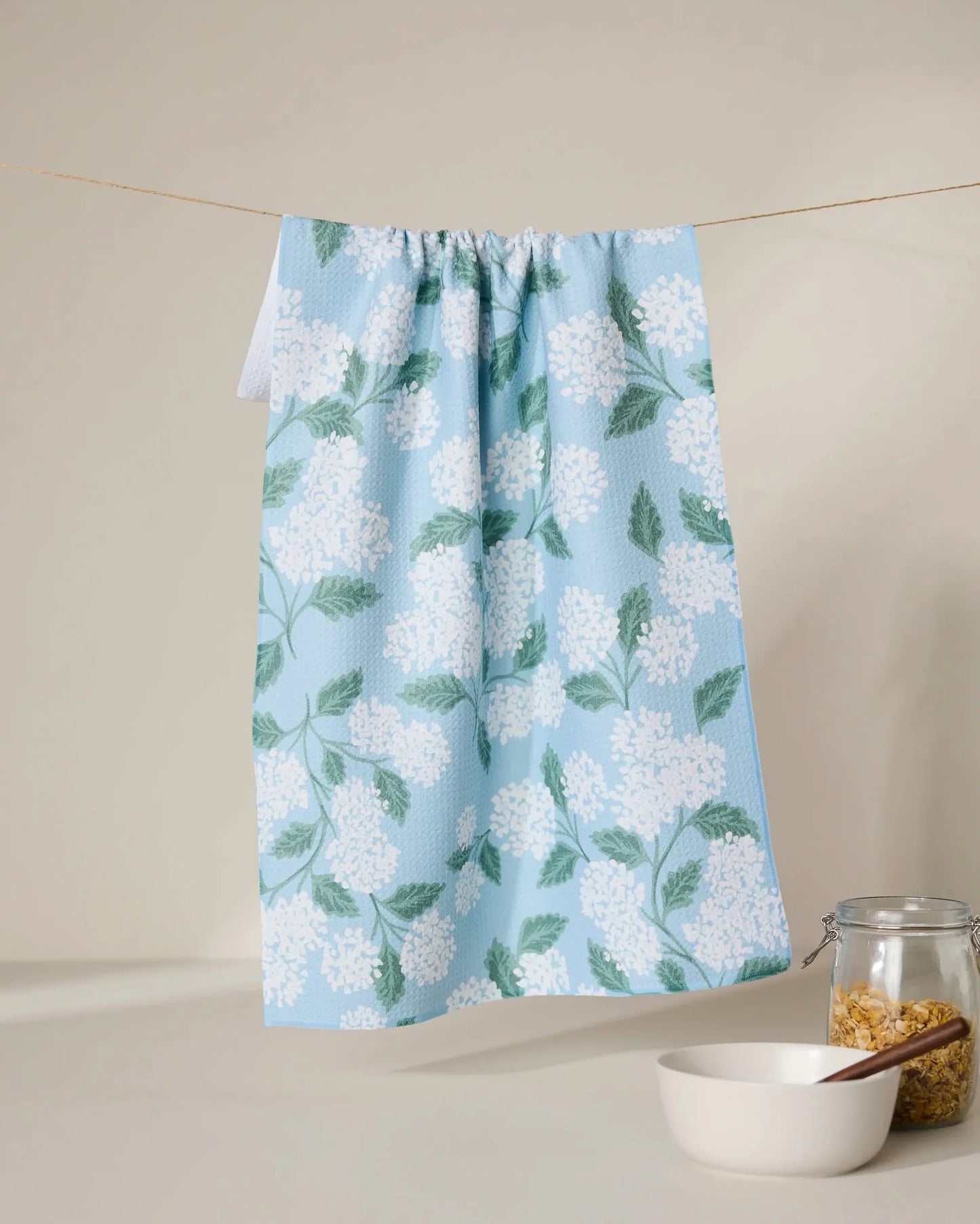 Floral-patterned towel hanging on a line with a bowl and jar in the foreground.