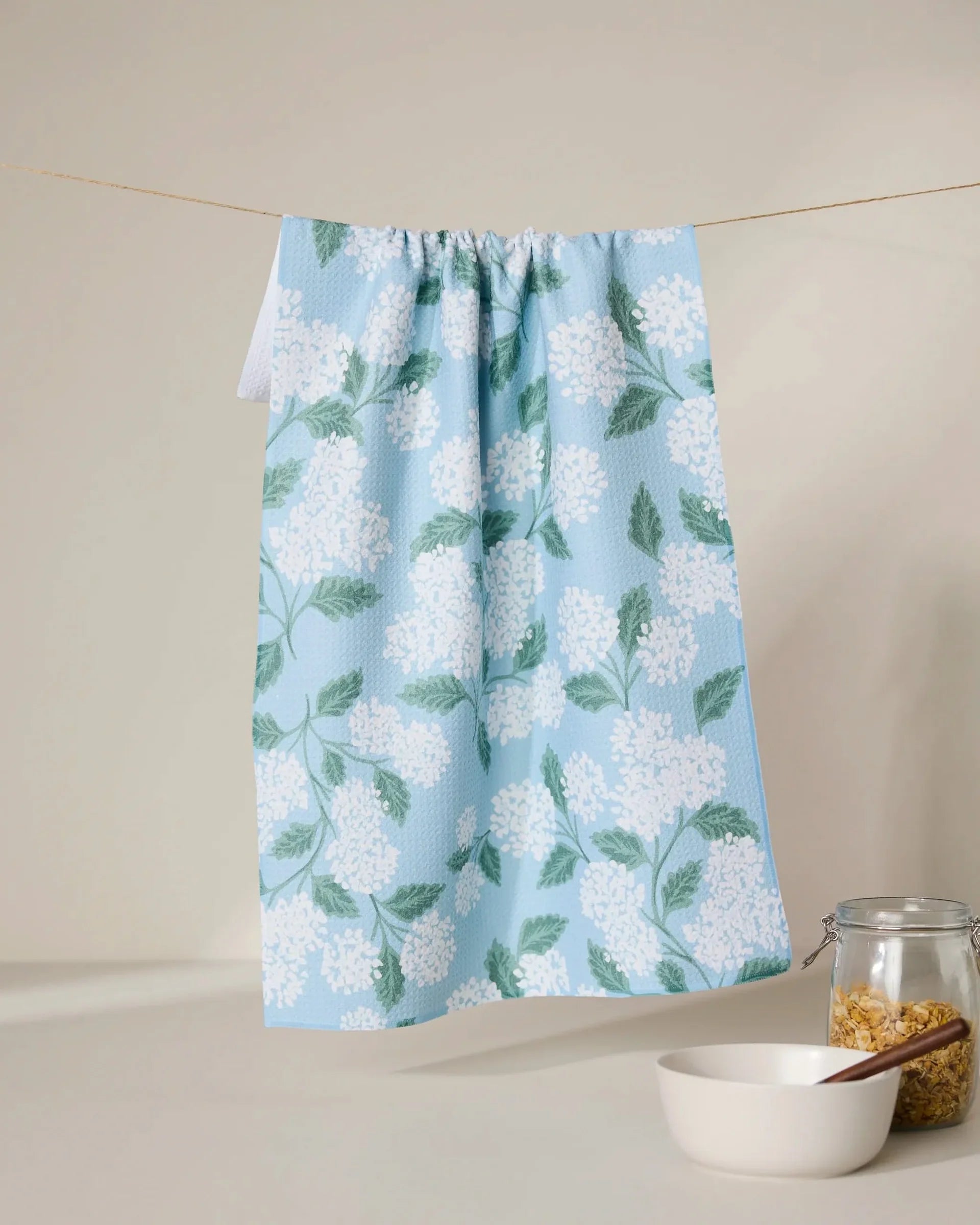 Floral-patterned towel hanging on a line with a bowl and jar in the foreground.