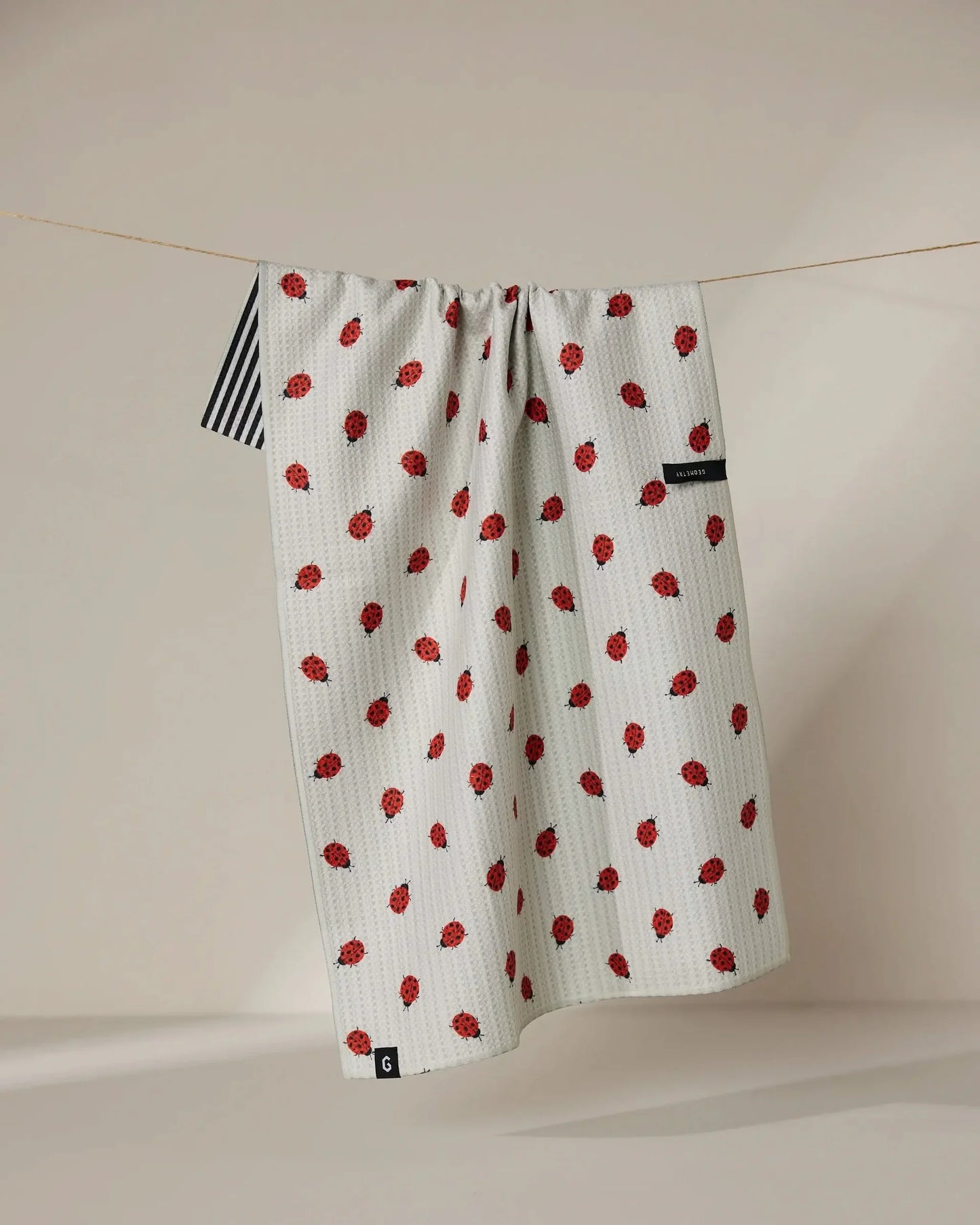 White towel with red pattern hanging on a line against a beige wall.