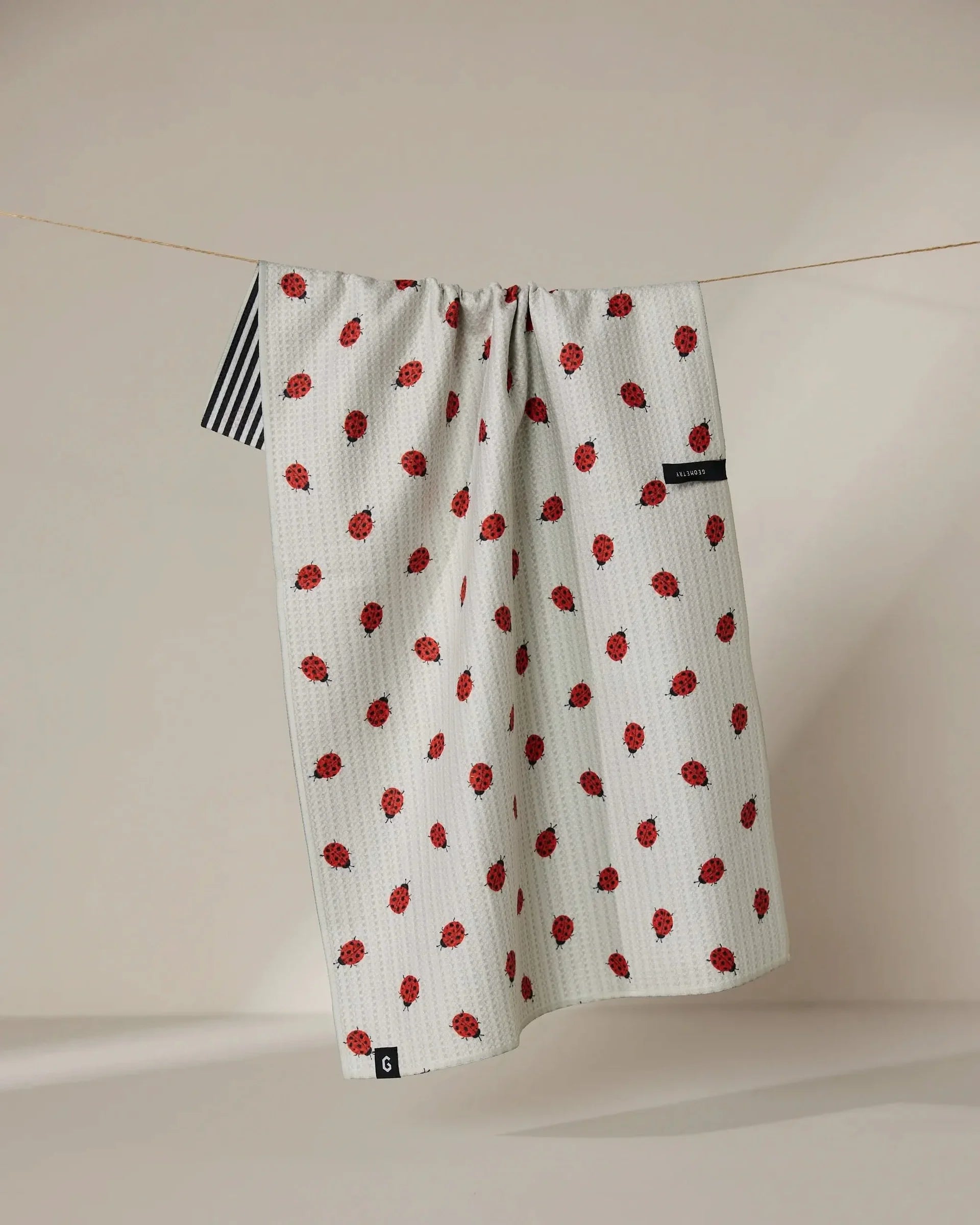 White towel with red pattern hanging on a line against a beige wall.
