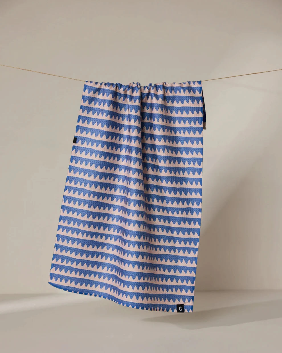 Blue and white patterned towel hanging on a line against a plain background