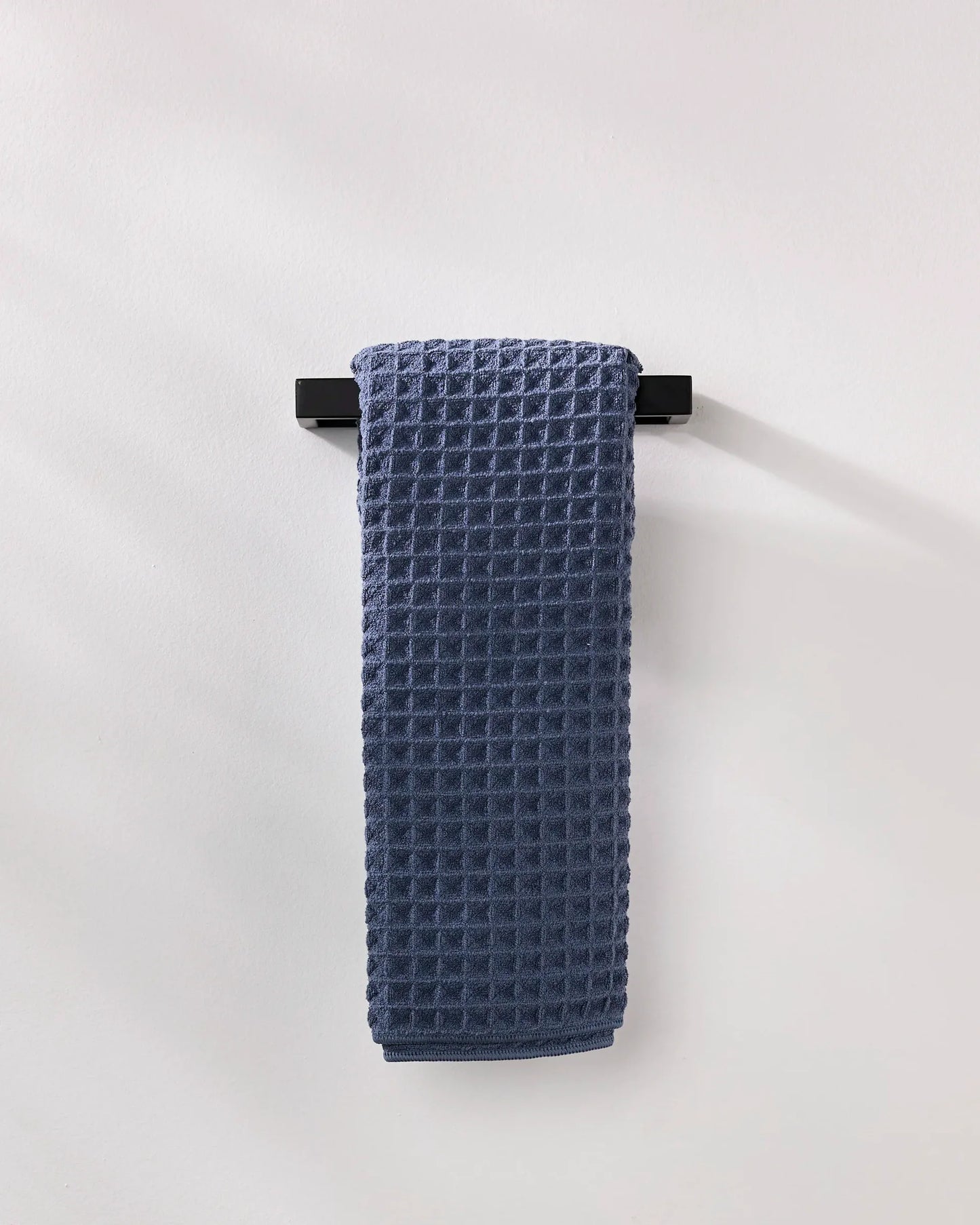 Blue waffle-textured towel hanging on a black rack against a white background