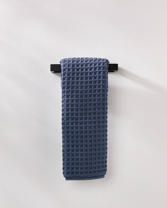 Blue waffle-textured towel hanging on a black rack against a white background