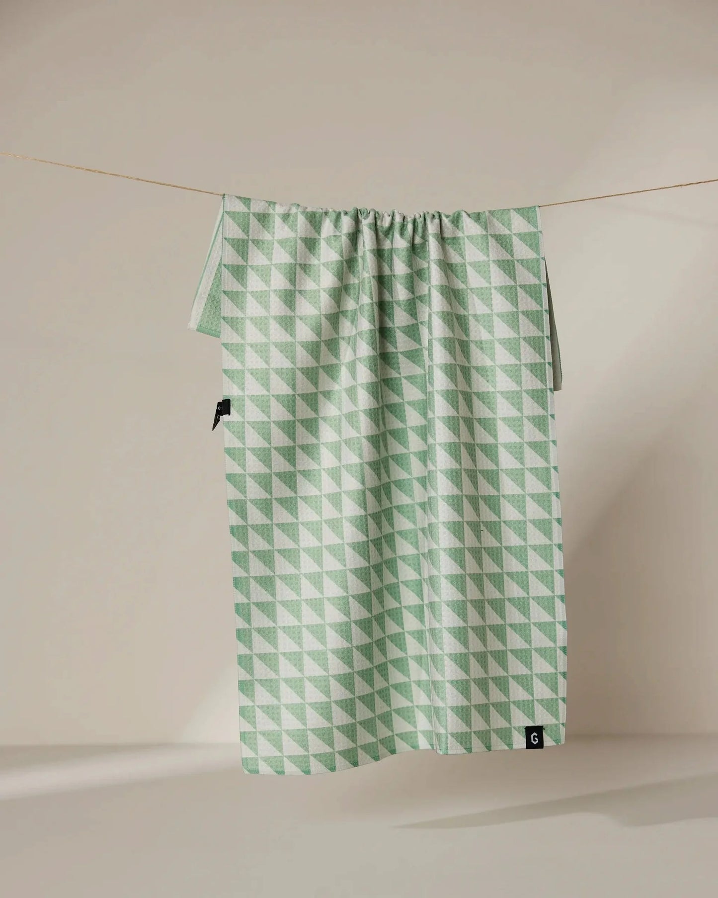 Green geometric patterned bag hanging on a line against a beige background