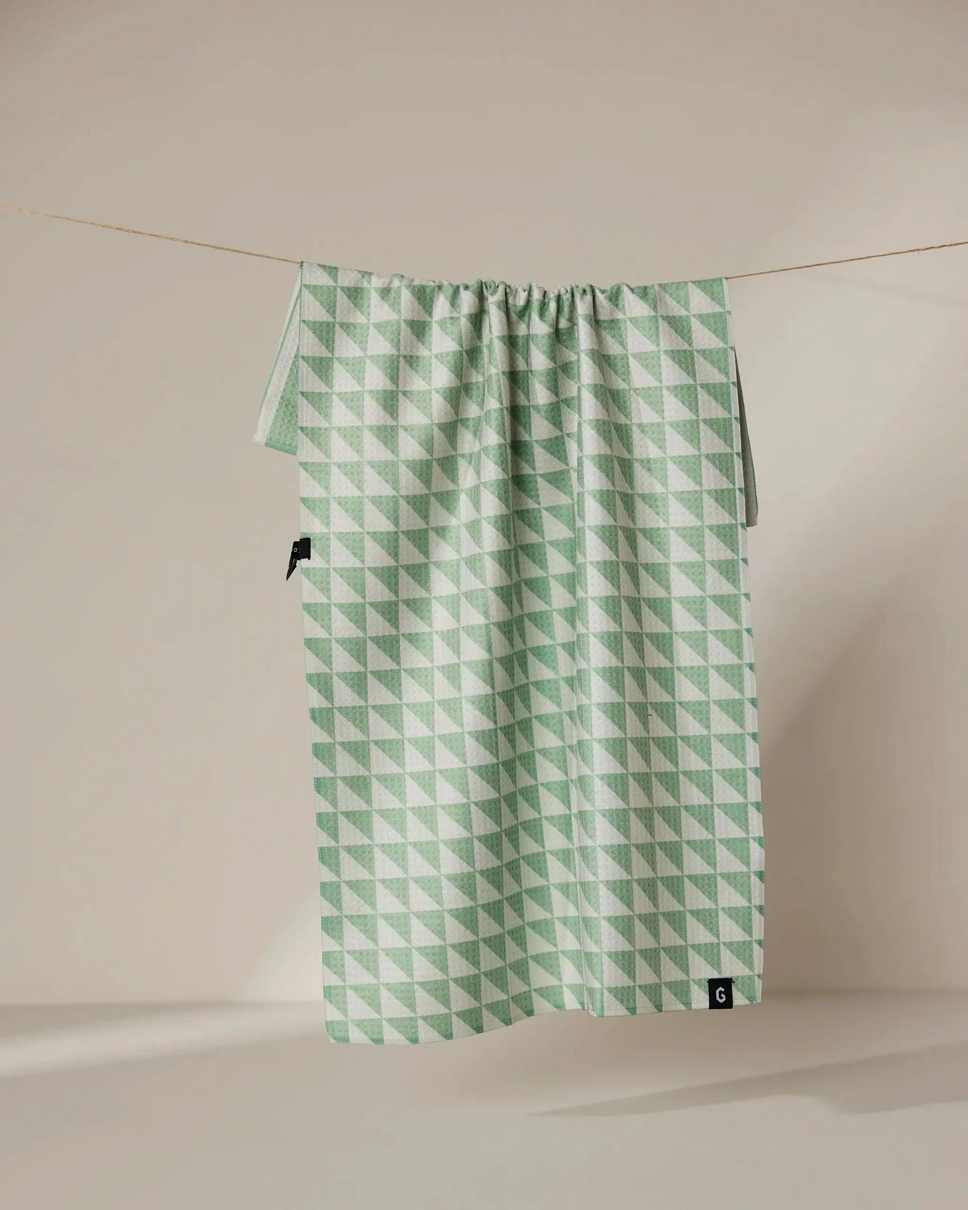 Green geometric patterned bag hanging on a line against a beige background