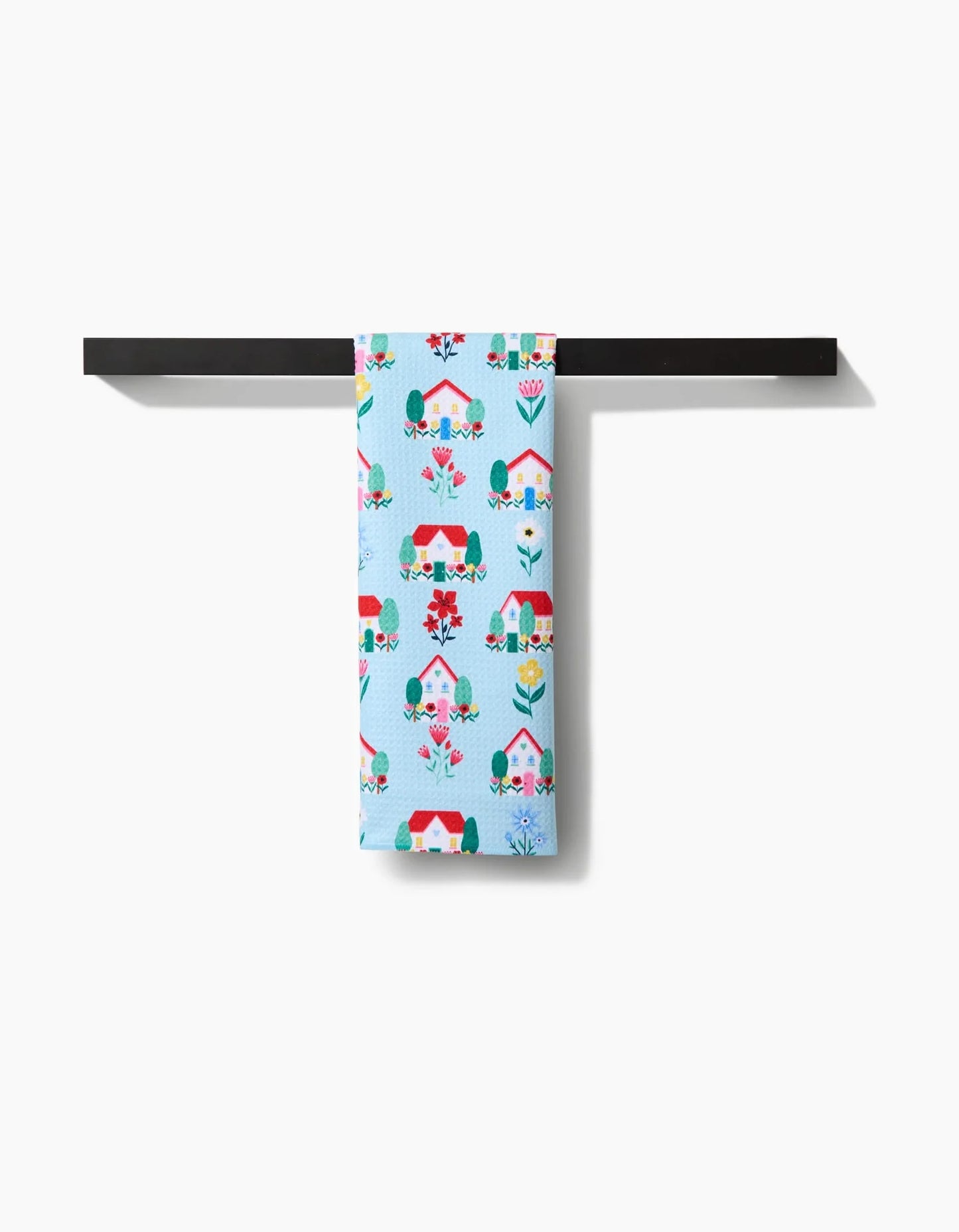 Towel with a colorful house pattern hanging on a black rod against a white background
