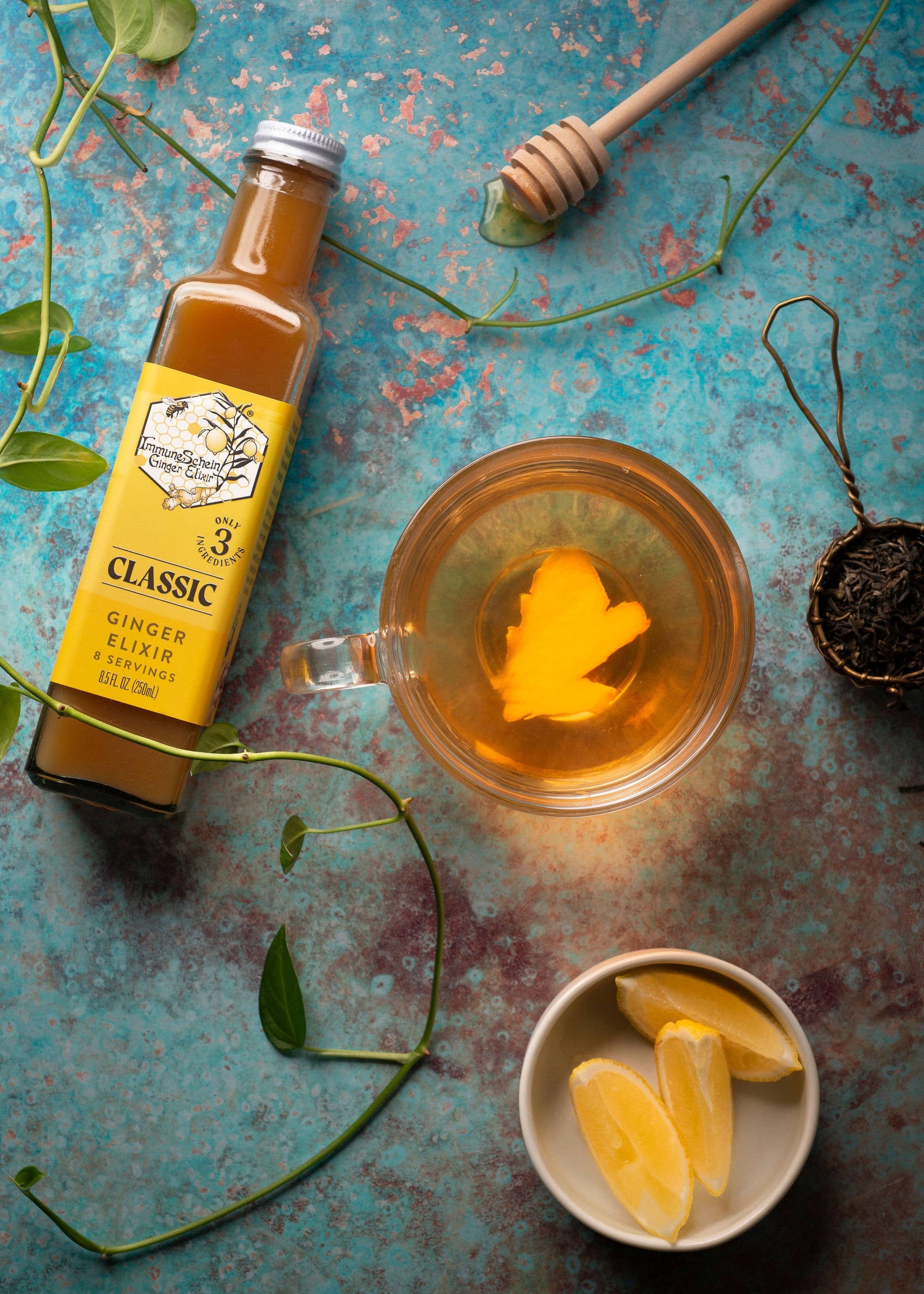 Bottle of ginger elixir with a glass of tea and lemon slices on a textured surface.