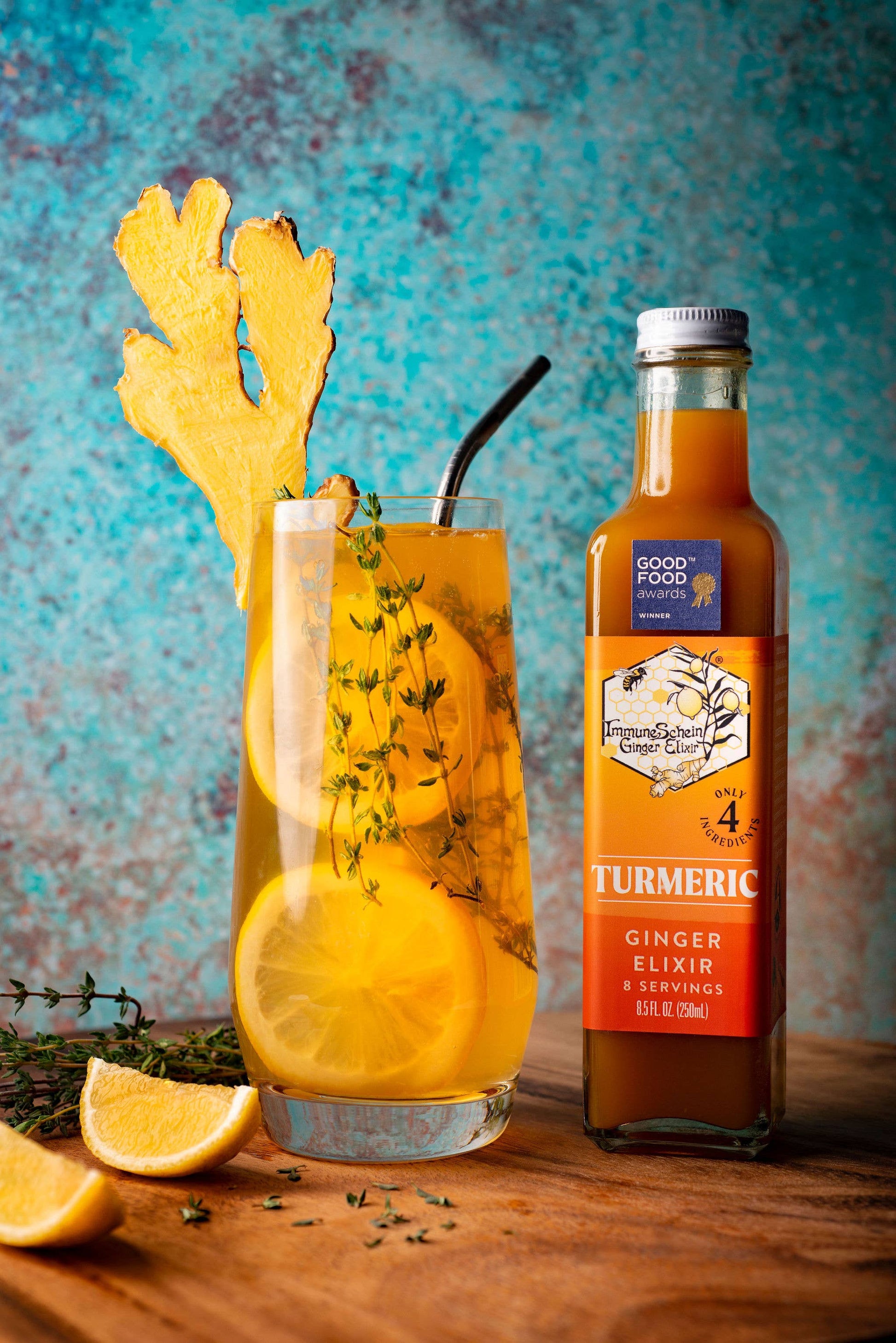 Turmeric ginger elixir bottle with a glass of iced tea on a wooden surface against a blue textured background.