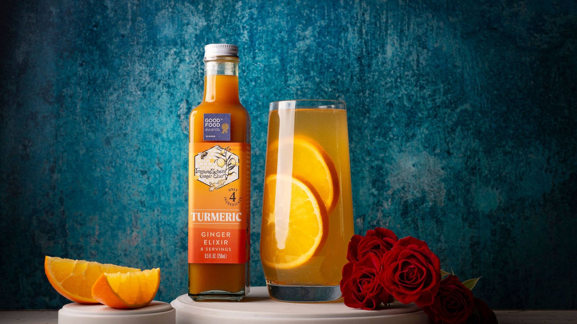 Bottle of Good & Gather Turmeric Ginger Juice with a glass of juice and orange slices on a blue textured background.
