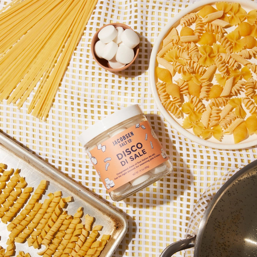 Jar of Jacobsen Salt Co. Disco di Sale with various types of pasta on a checkered tablecloth.