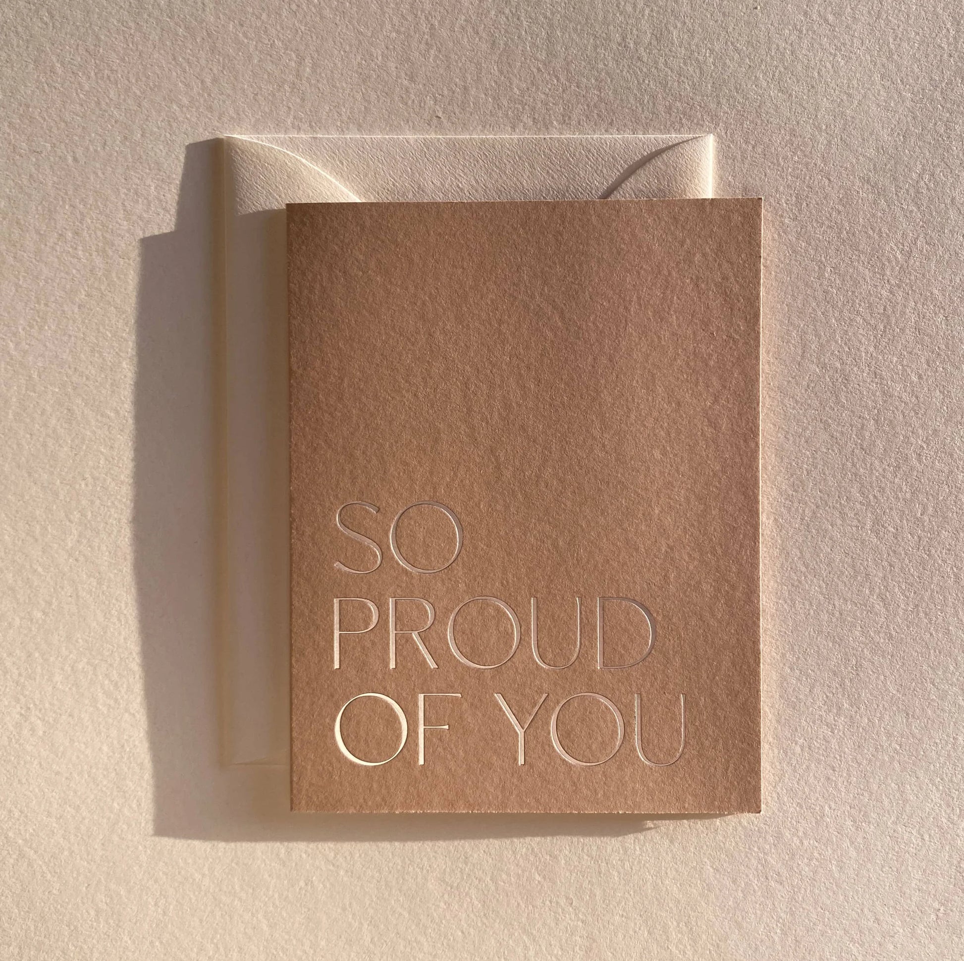Brown greeting card with 'So Proud of You' text on a beige background