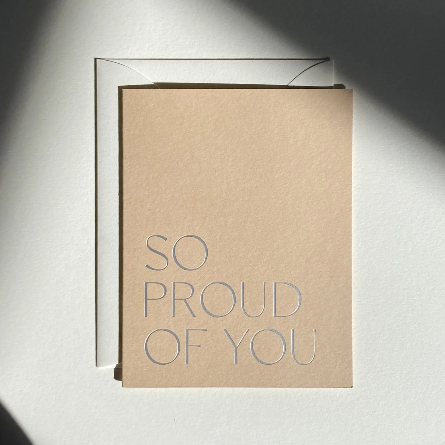 Kraft paper card with 'SO PROUD OF YOU' text on a light gray background