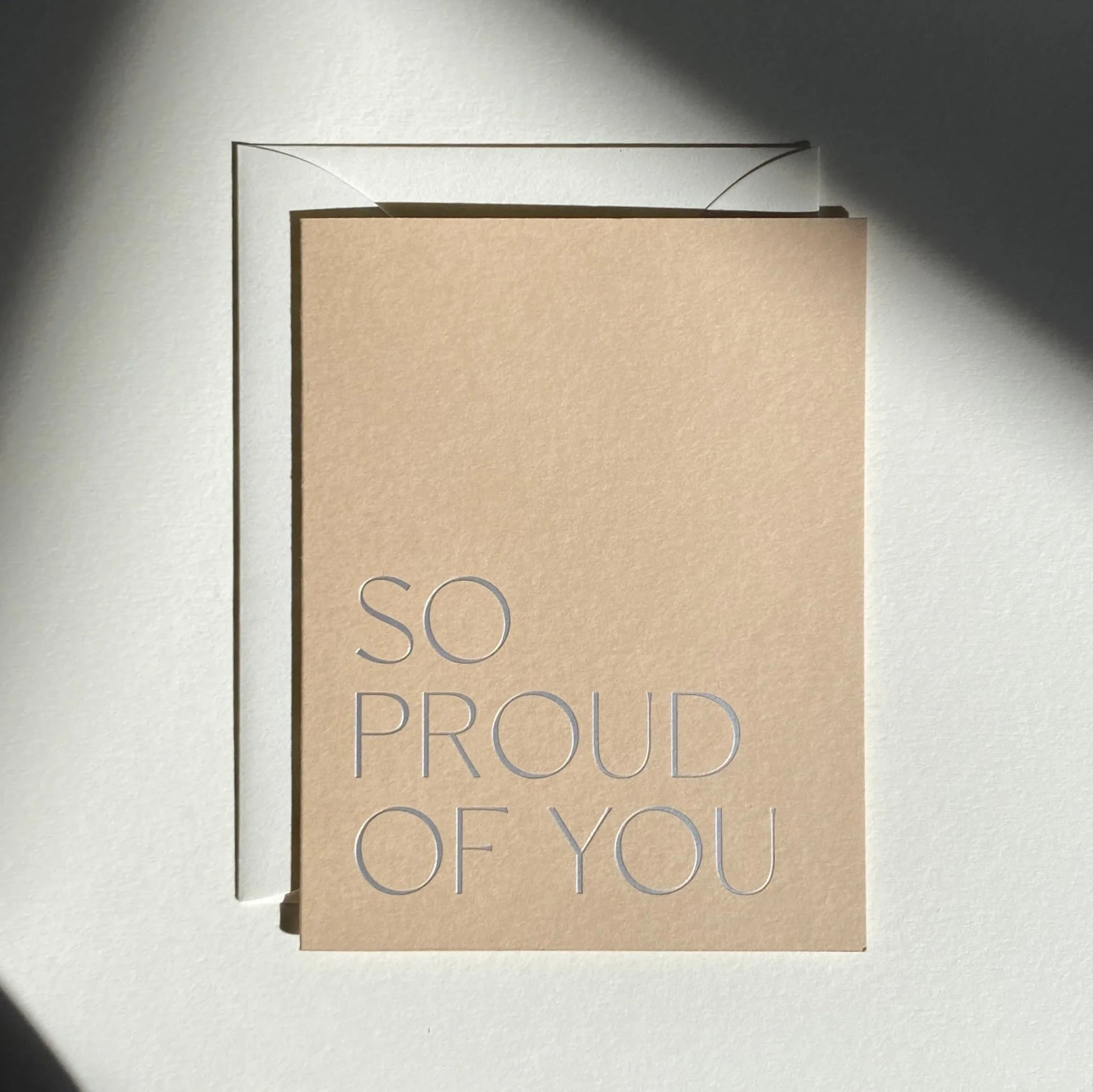 Kraft paper card with 'SO PROUD OF YOU' text on a light gray background