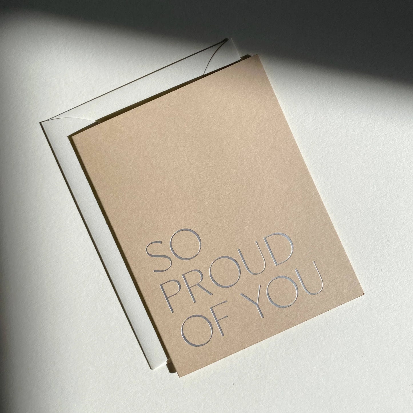Kraft paper card with 'So proud of you' text on a light background