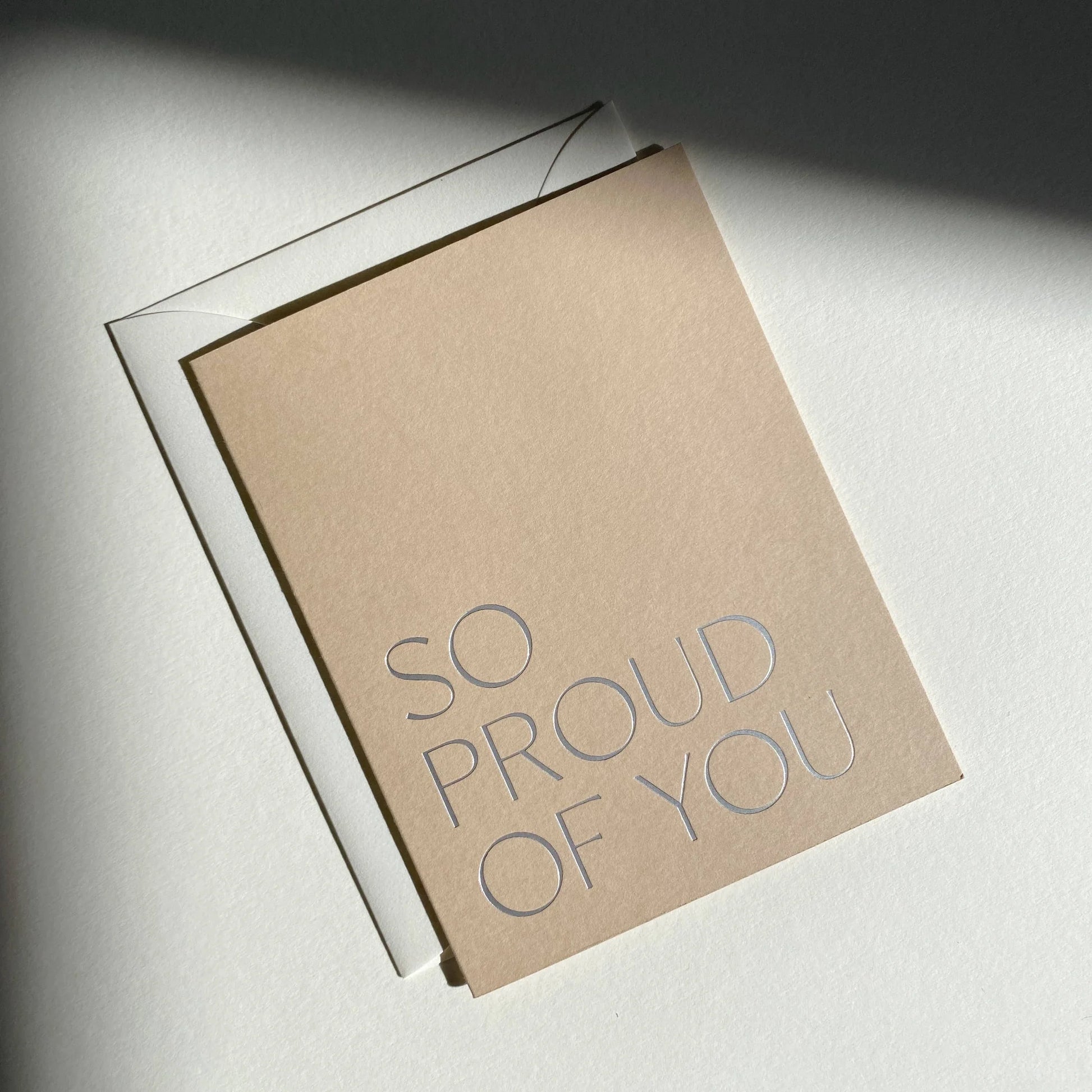Kraft paper card with 'So proud of you' text on a light background