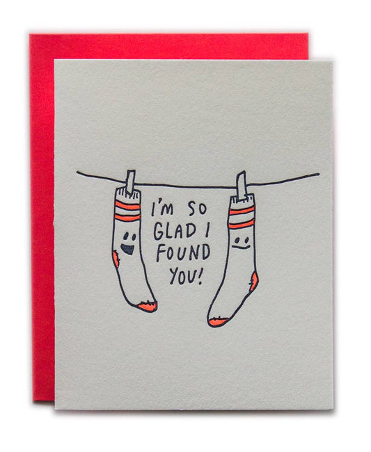 Card with socks on a clothesline and text 'I'm so glad I found you!' against a red and gray background.