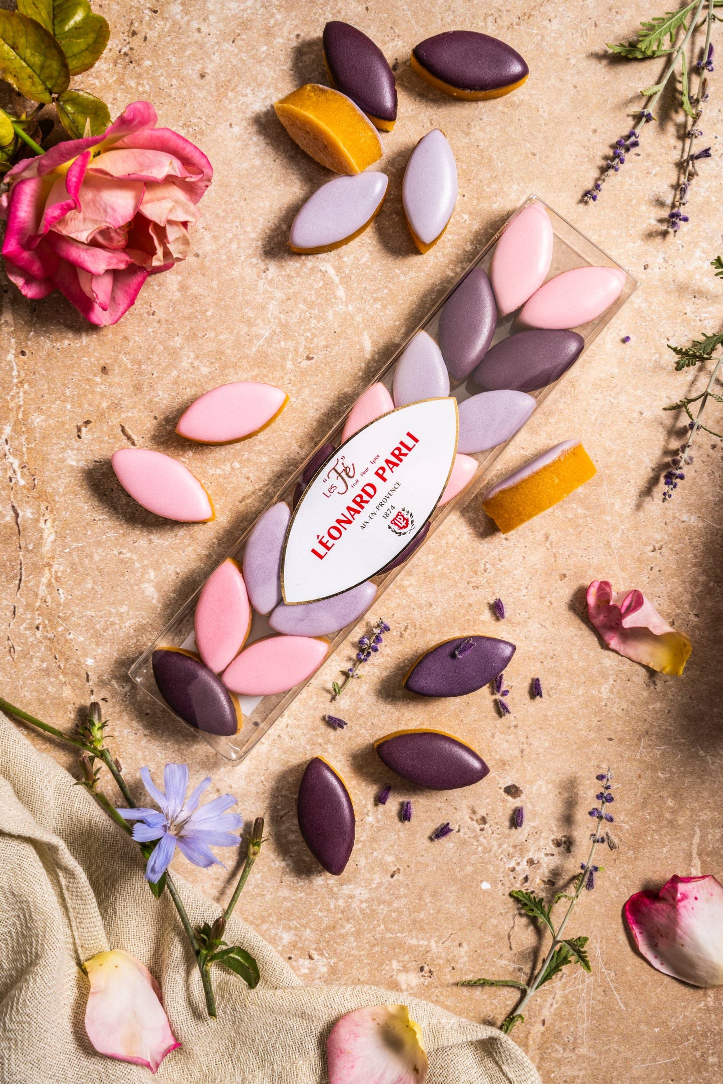 Colorful chocolate candies on a textured surface with flowers and herbs