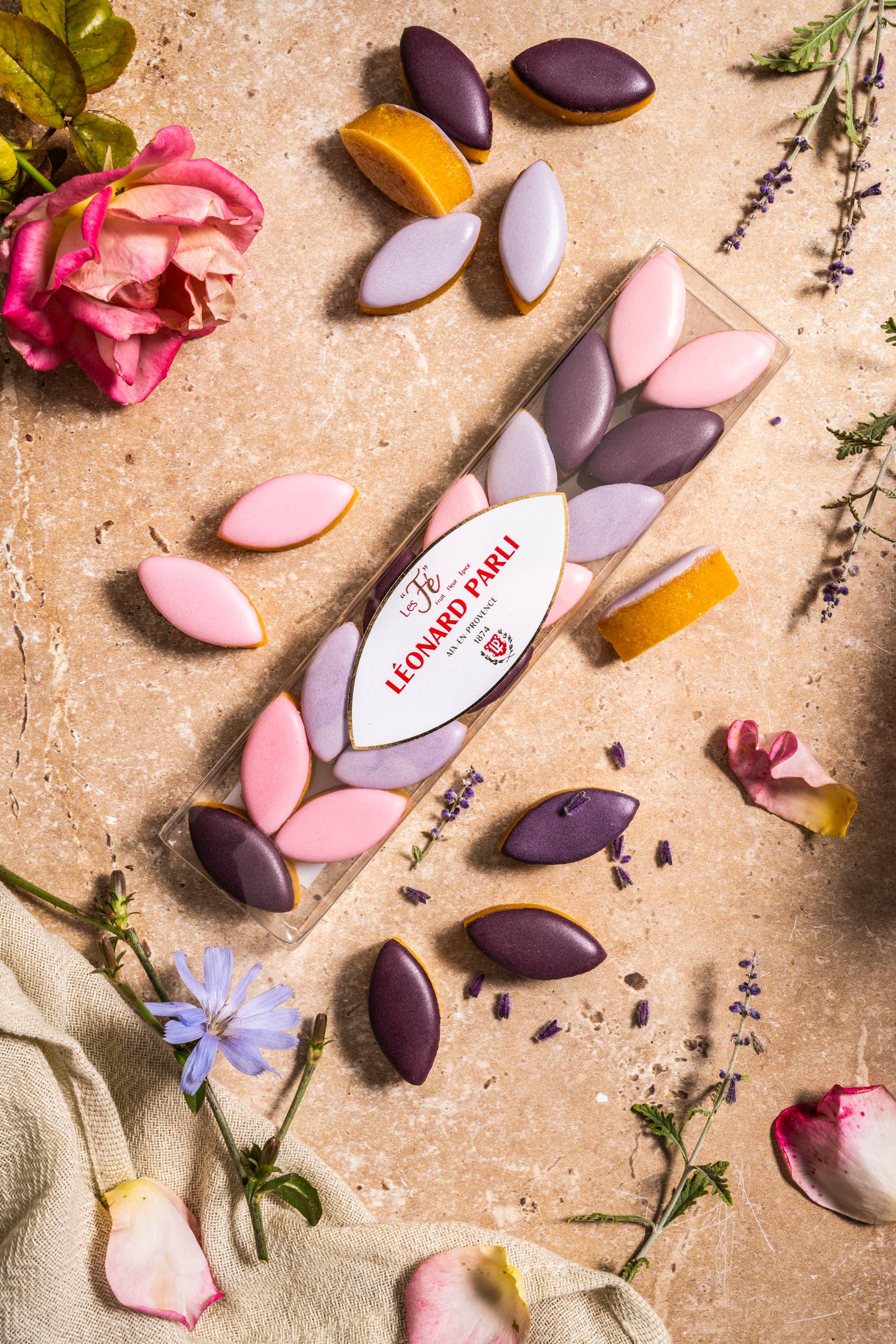 Colorful chocolate candies on a textured surface with flowers and herbs