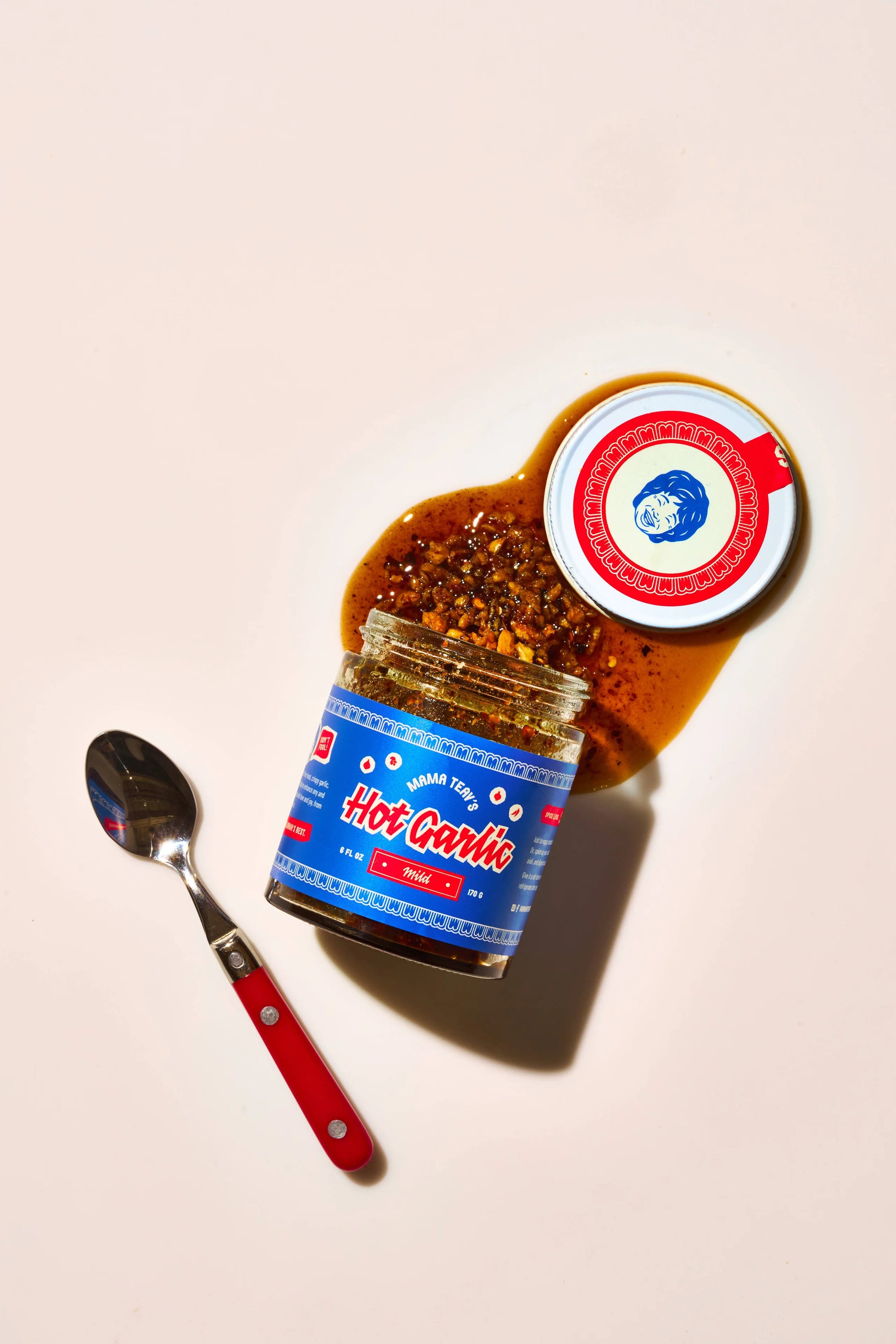 Jar of hot garlic with a red and white label and a spoon on a beige background
