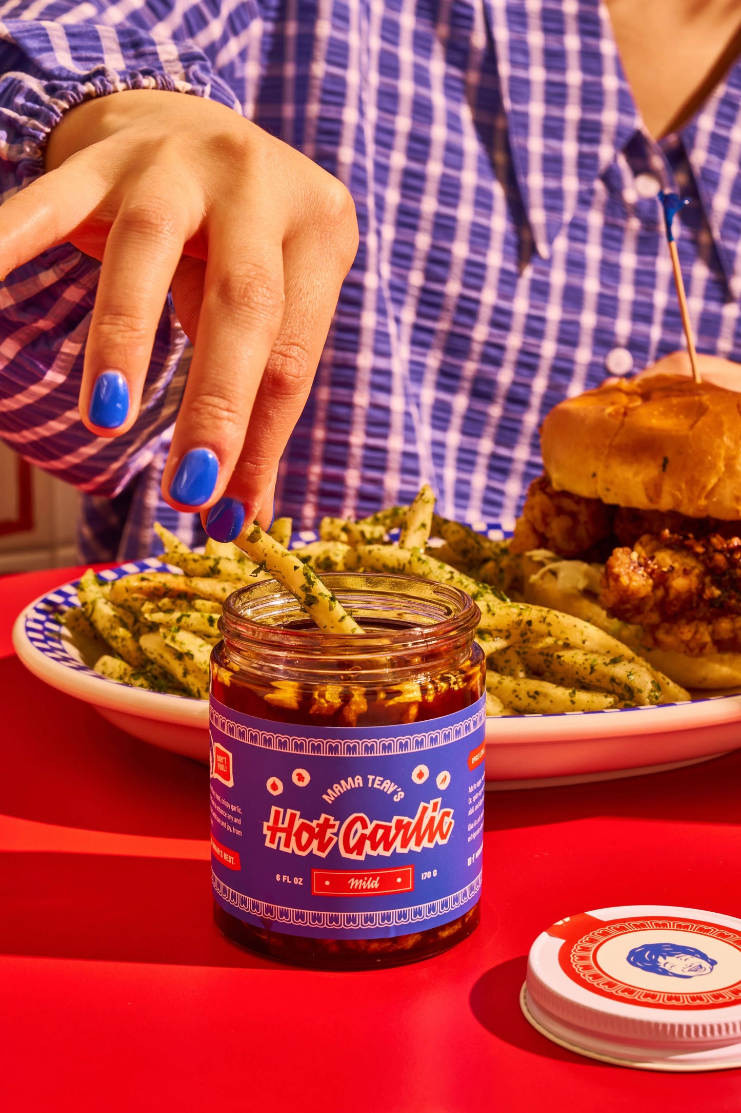 Person reaching for a jar of 'Hot Garlic' sauce on a table with food.