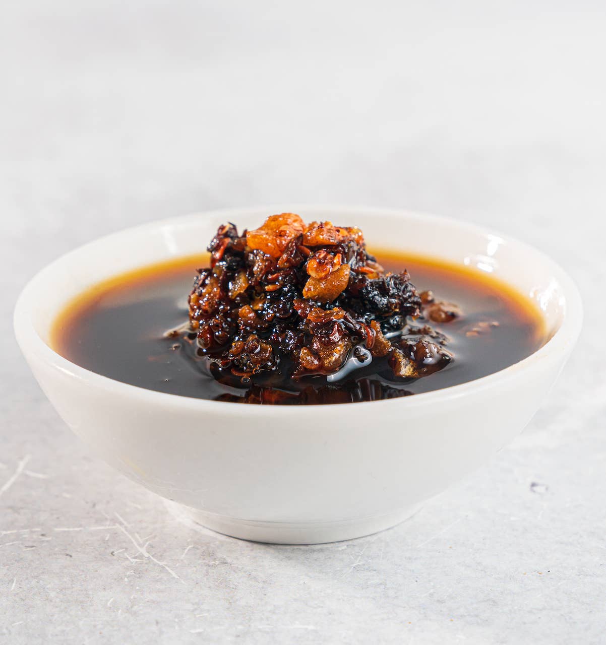 White bowl with dark sauce and chunks of food on a light gray background