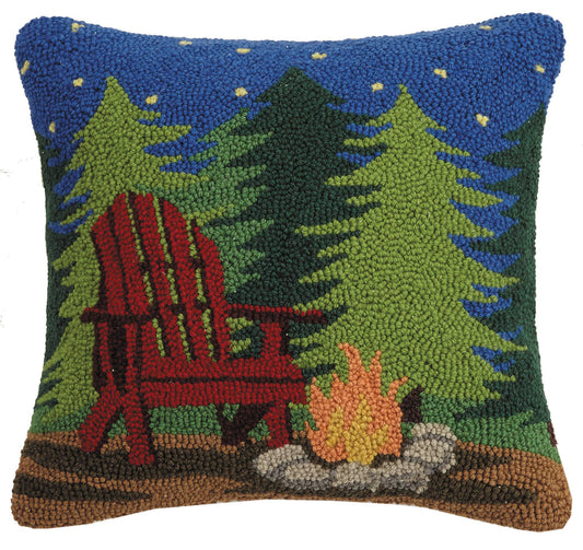 Decorative pillow with a red Adirondack chair, campfire, and trees on a blue background